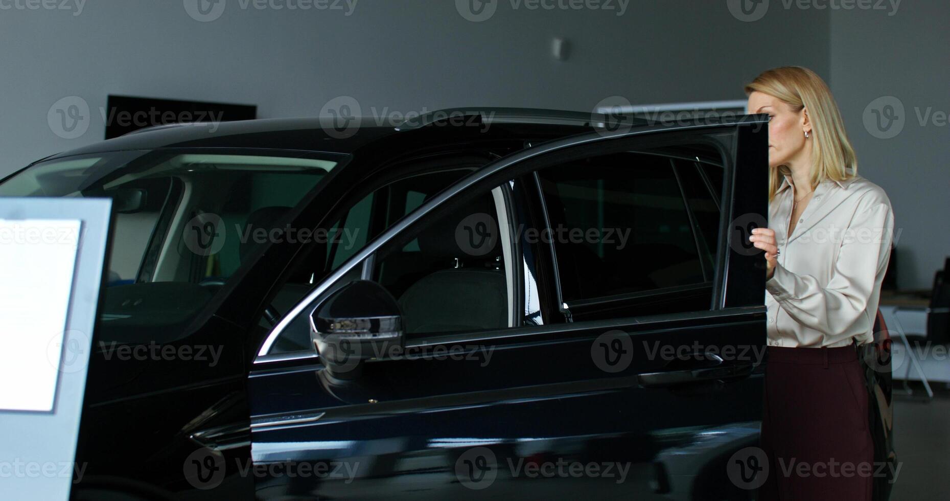 A stylish woman chooses a car by walking around the showroom of a car dealership with a thoughtful look and looking into cars photo