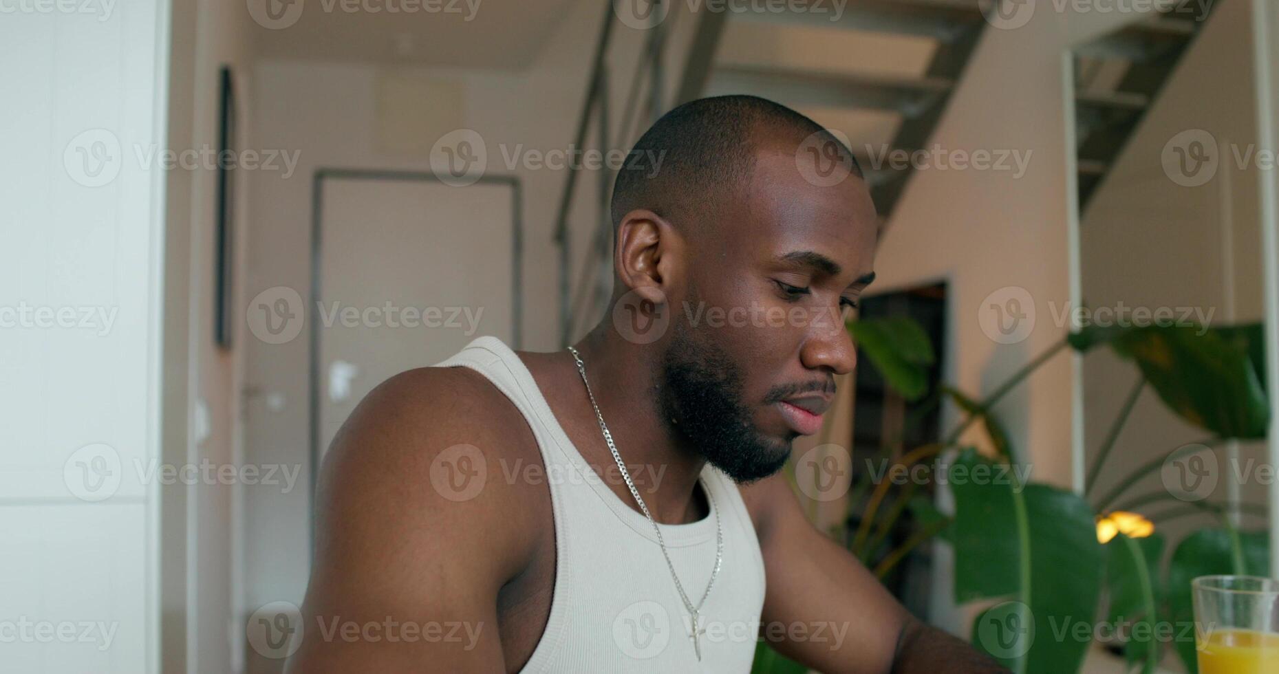 A man in pajamas uses a laptop and writes in a notebook sitting at a table in the kitchen at home with a serious look - notebook photo