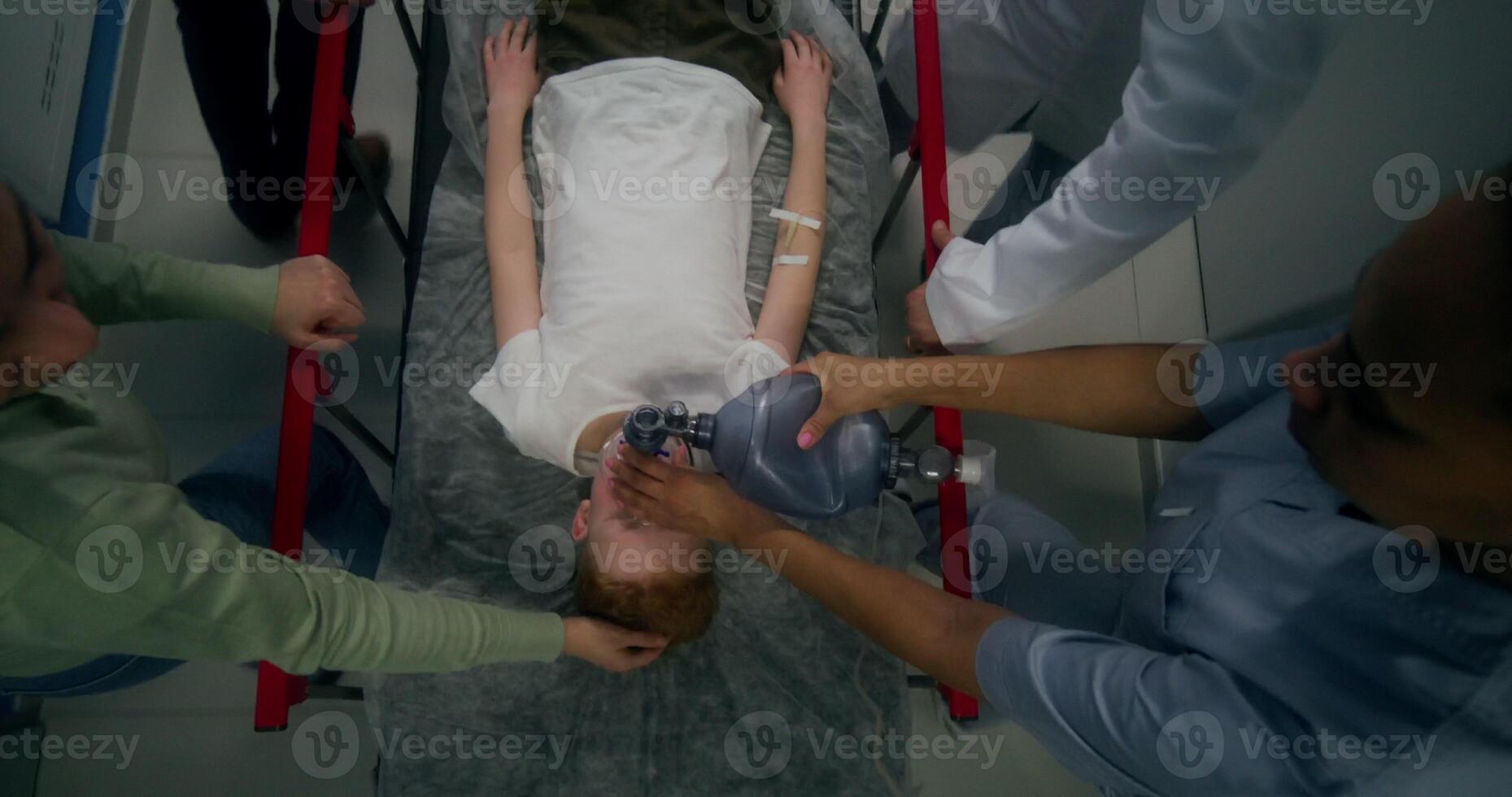 Medical staff and parents carry the boy on a gurney, giving him oxygen with a mask, top view - giving photo