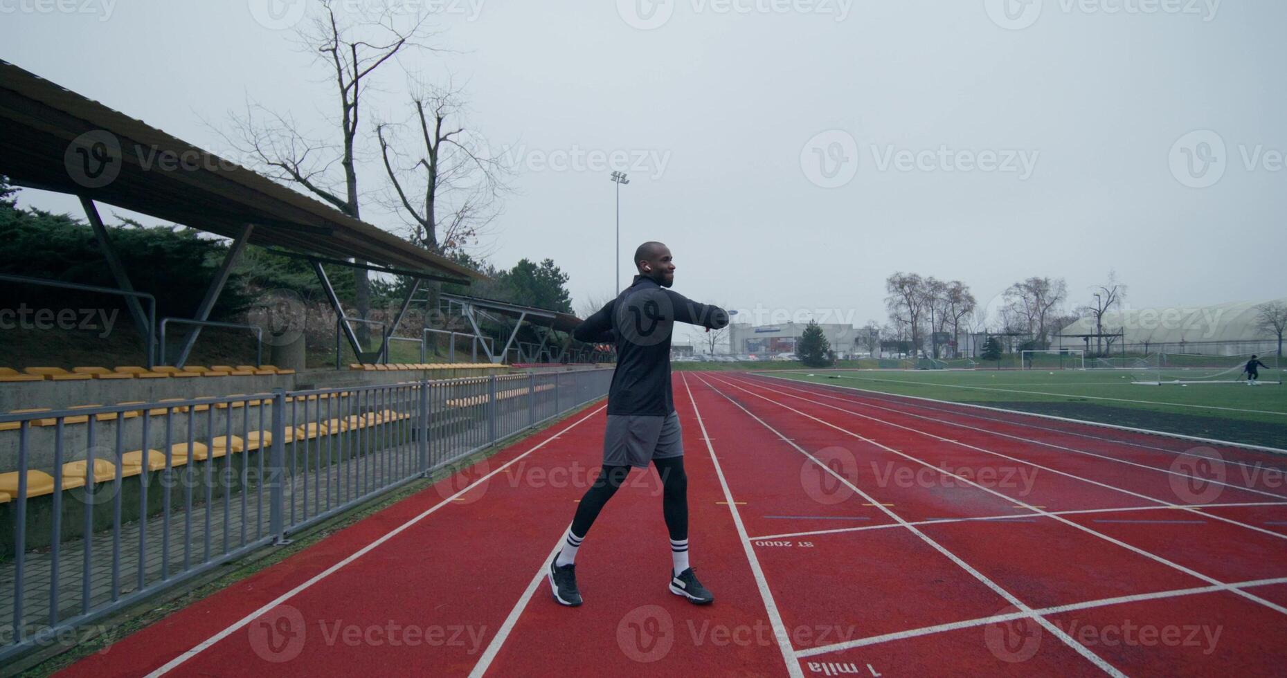 A man in a sports outfit with earphones in his ears does a warm-up standing at the stadium on a cold day - earphones photo