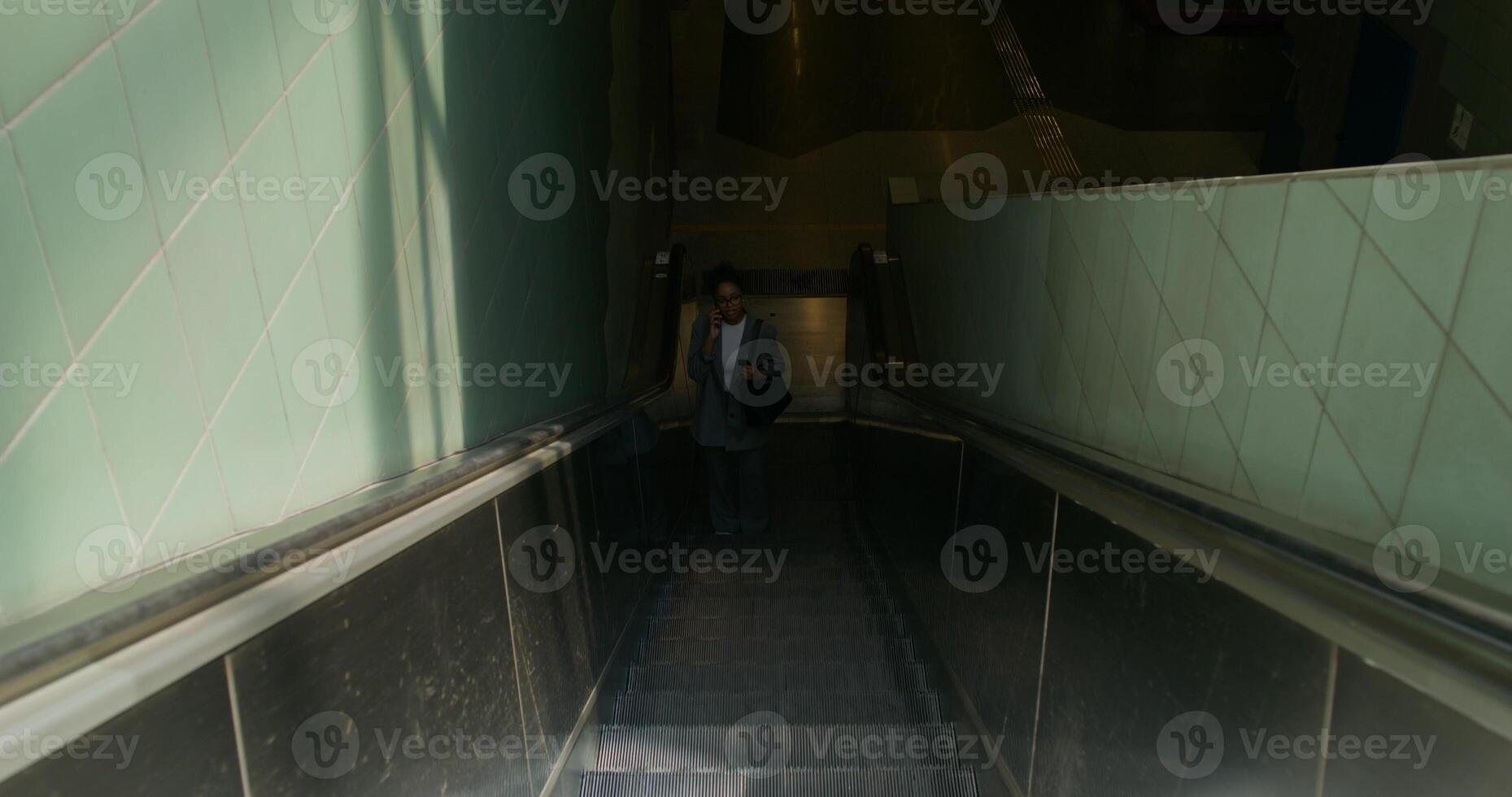 A woman in formal clothes is talking on a mobile phone. She rides the escalator coming up from the subway station - escalator photo