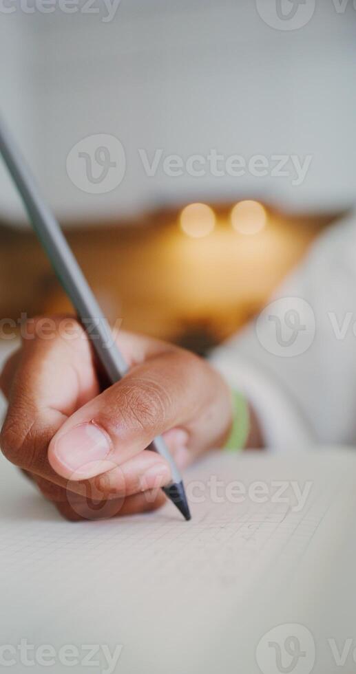 A child's hand is writing in a notebook, a girl is doing homework sitting at a table in the kitchen, close-up of her hand - writing photo