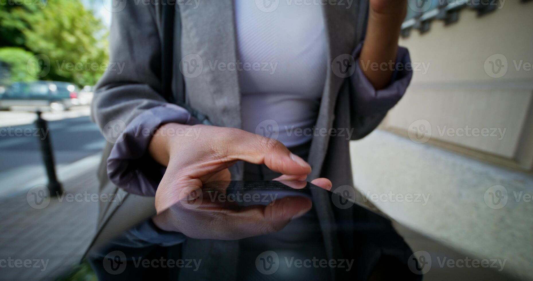 A woman in formal clothes uses a mobile phone walking along a city street. She holds a disposable cup of coffee in her hand. Close-up of a mobile phone screen, an unrecognizable person photo