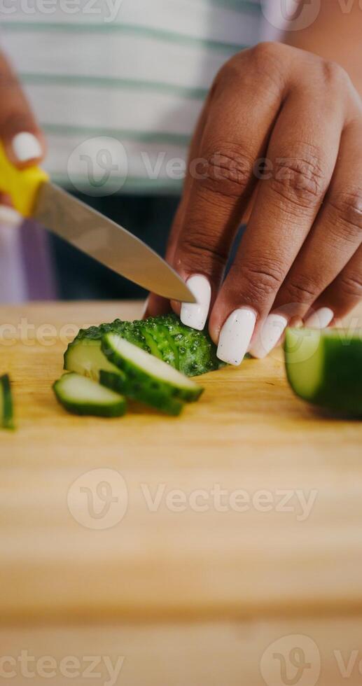 Women's hands are cutting a cucumber while preparing a salad in the kitchen, there is no face photo