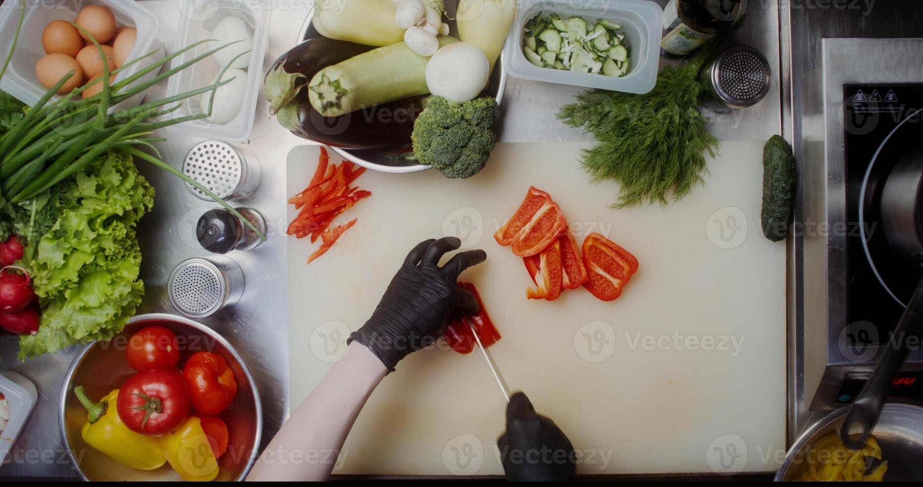A woman in disposable black gloves cuts peppers standing near a table full of vegetables, close-up of her hands, top view - standing photo