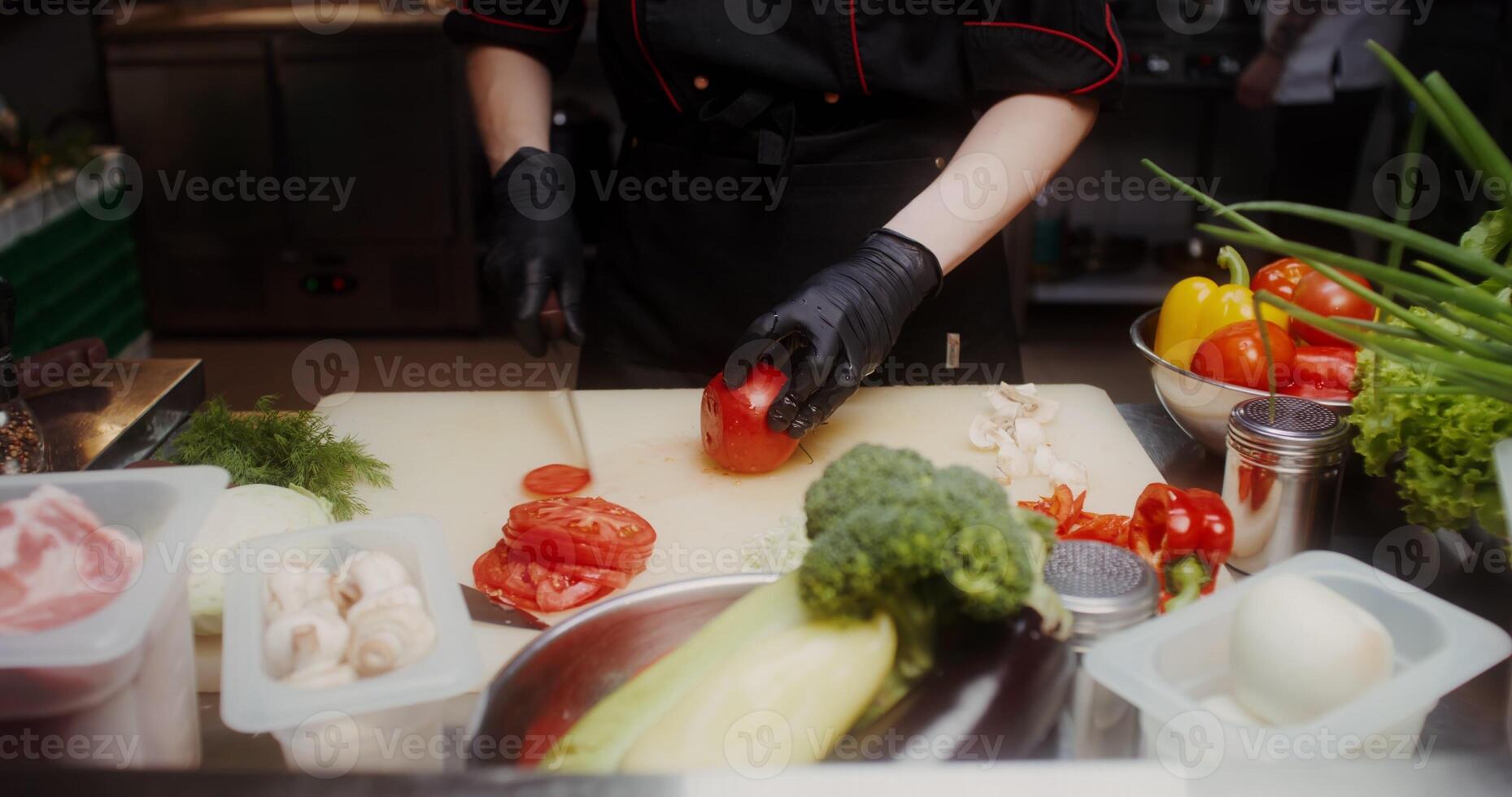 A woman in a chef's uniform with disposable black gloves on her hands cuts vegetables standing in the restaurant kitchen. Close-up of a woman's hands, no face - gloves photo