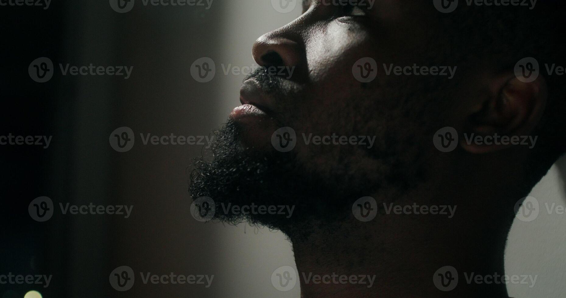 A bearded man in casual clothes leaned his head against the wall with a depressed look, close-up of his face. Dim indoor lighting - clothes photo