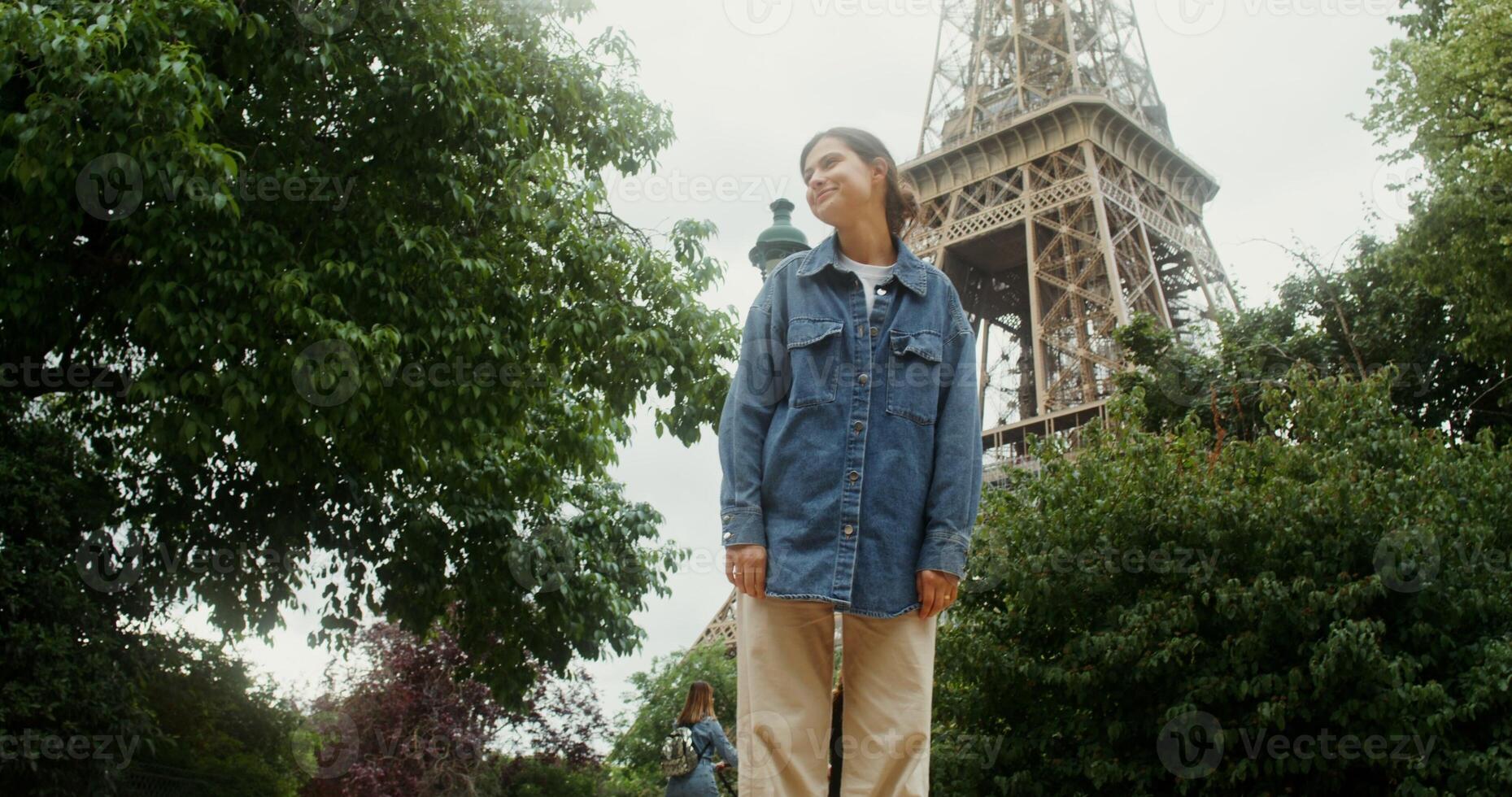 A young beautiful woman smiles and spins around herself, standing in the park on the Champ de Mars at the foot of the Eiffel Tower on a sunny summer day. France Paris. 4k , red komodo - around photo