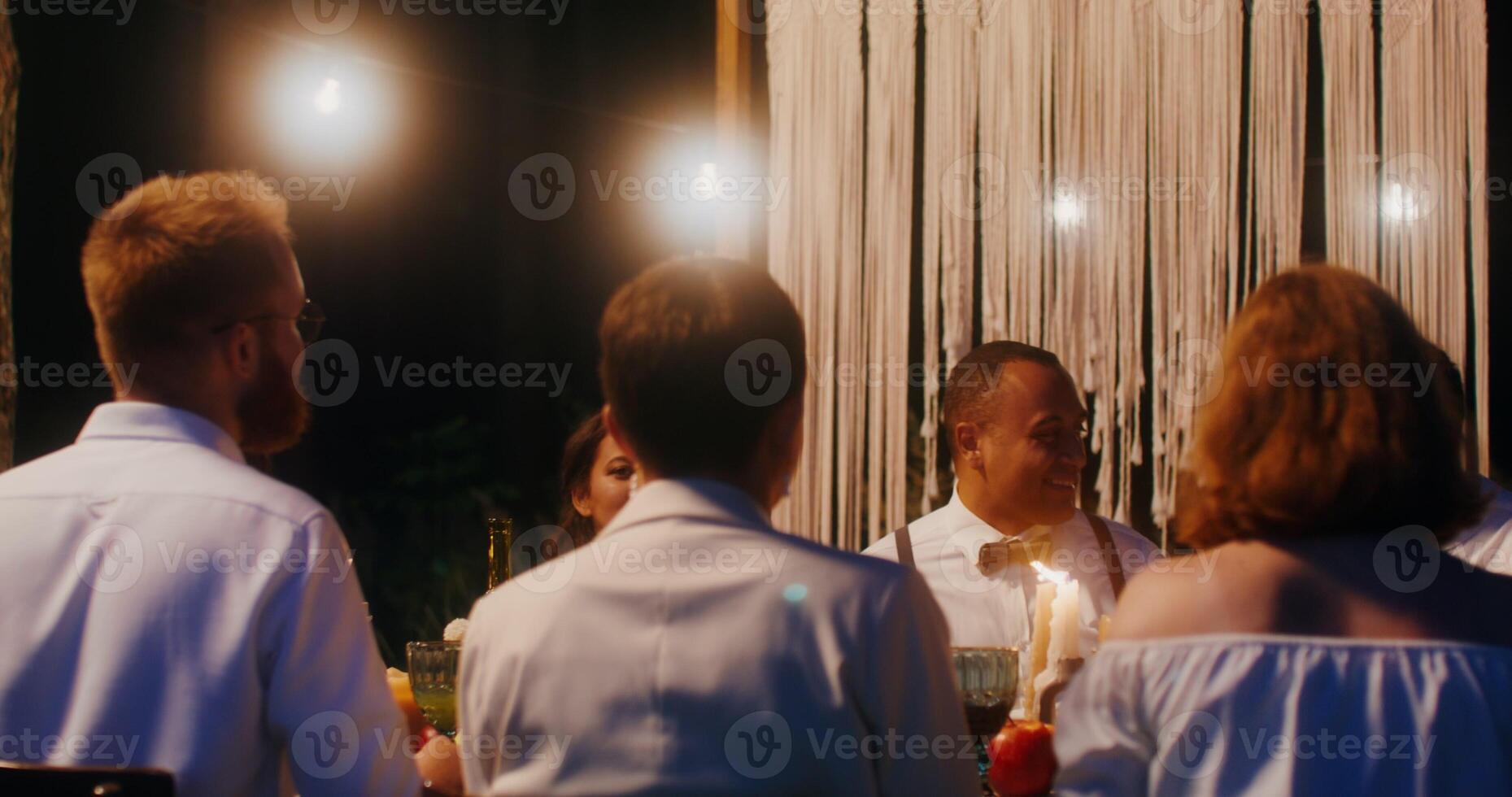 The bride and groom kiss standing up from behind the covered festive table, at which the guests are sitting - covered photo