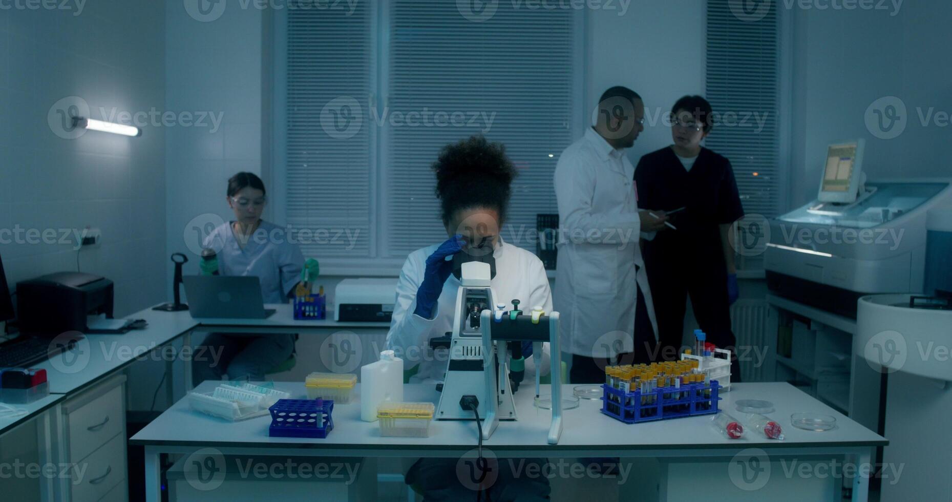 A group of laboratory technicians perform a blood test in the laboratory. A man and a woman use a tablet standing near a laboratory assistant's desk with a microscope - tablet photo