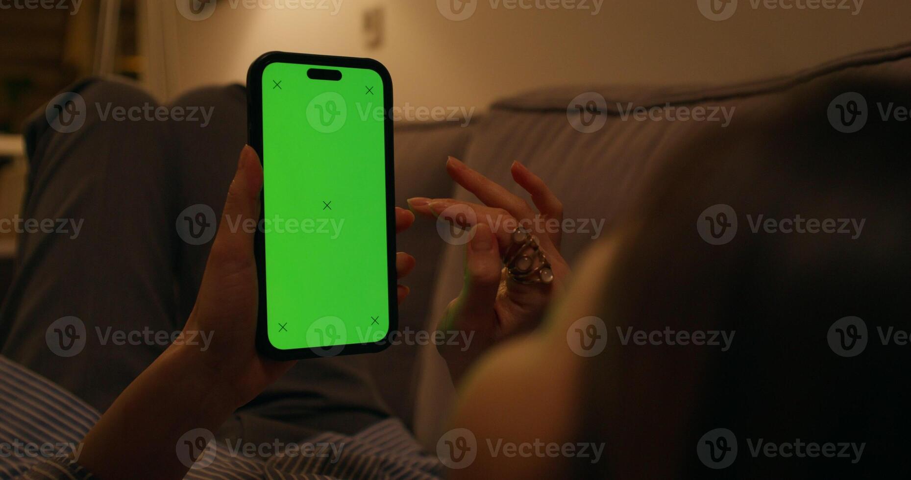 A woman uses a mobile phone with a green screen lying on the couch at home, an unrecognizable person - unrecognizable photo