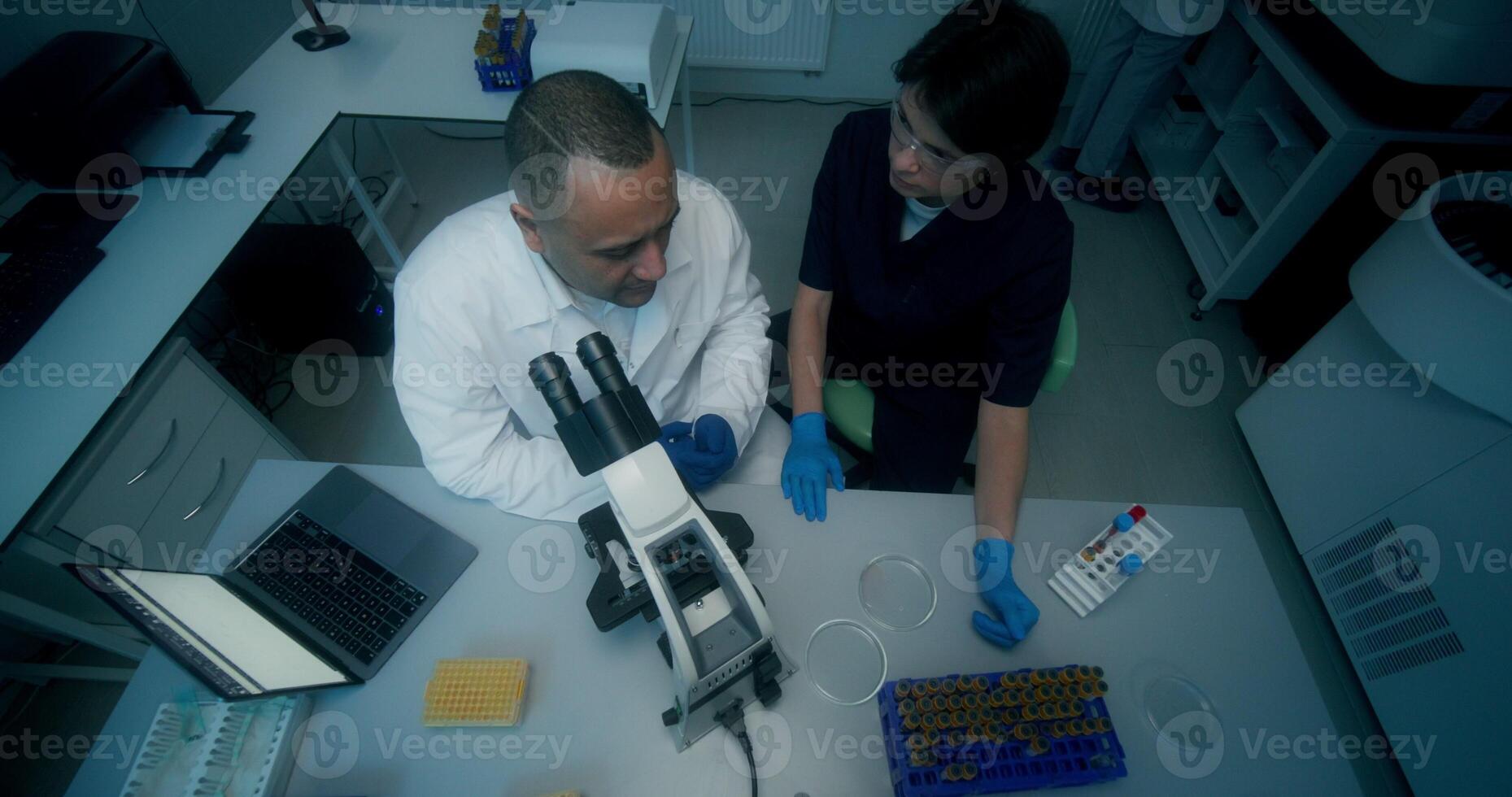 A man and a woman in lab coats are working in a medical laboratory, conducting a blood test and using a microscope. They are talking sitting at the table - working photo