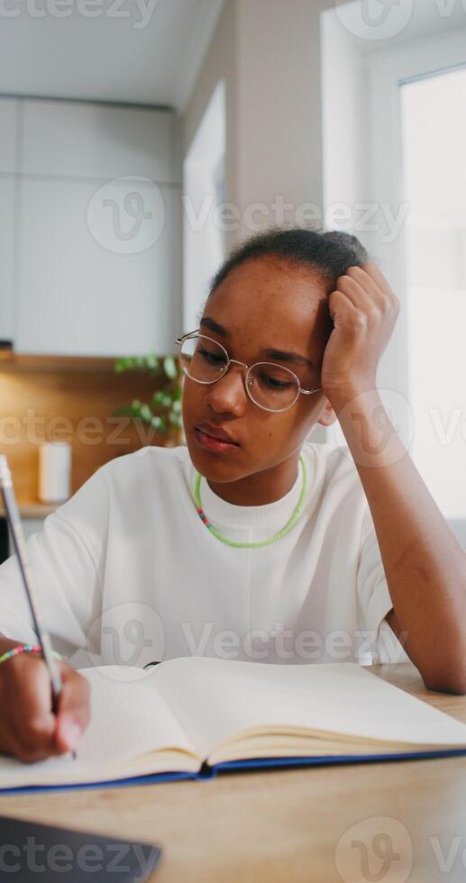 The girl does her homework at home, she uses a laptop and makes notes in a notebook while sitting at the kitchen table photo