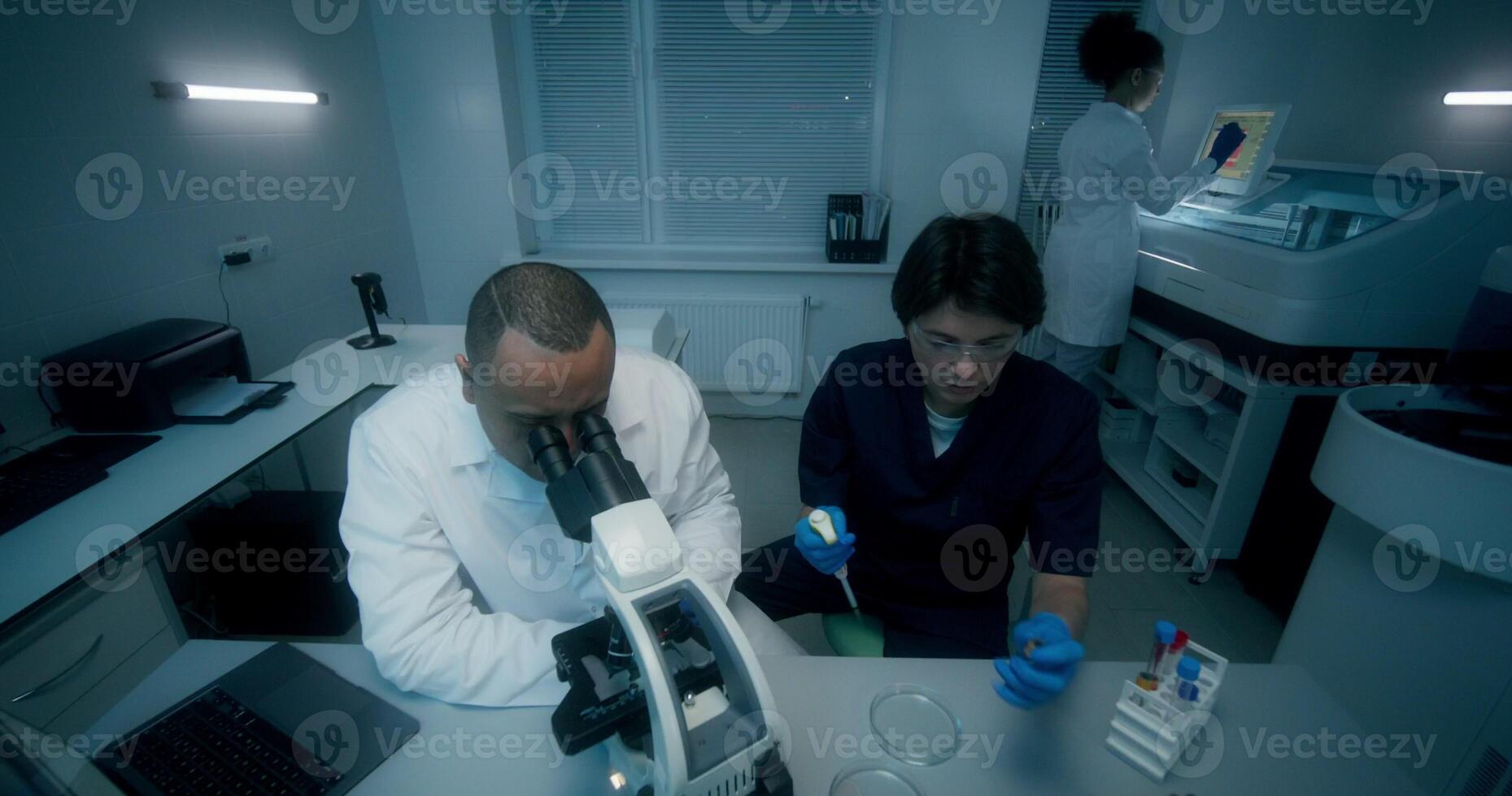 A man and a woman in lab coats are working in a medical laboratory, conducting a blood test and using a microscope. They are talking sitting at the table - conducting photo