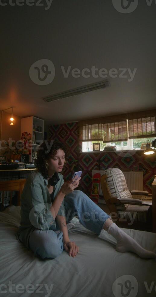 A young woman uses a mobile phone while sitting on a bed at home with a depressed look - depressed photo