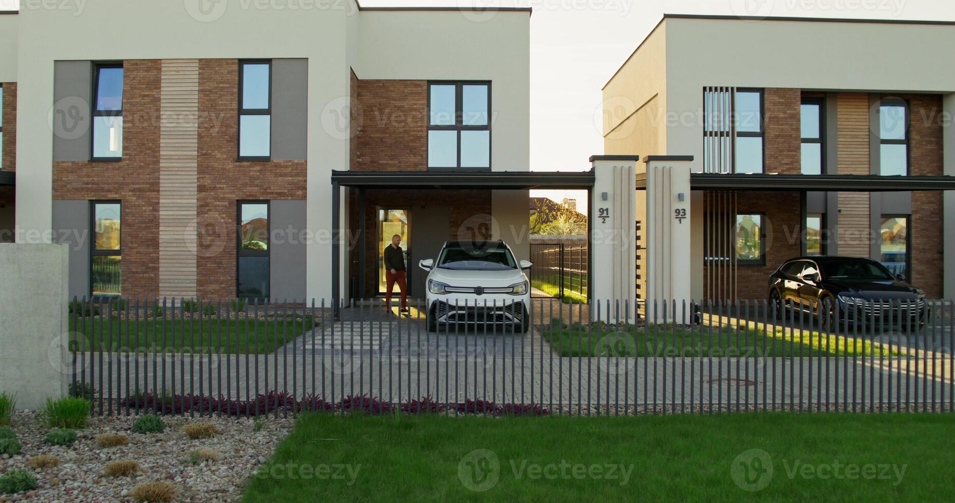 A man in casual clothes disconnects charging from an electric car parked in front of a stylish cottage. A sunny day - disconnects photo