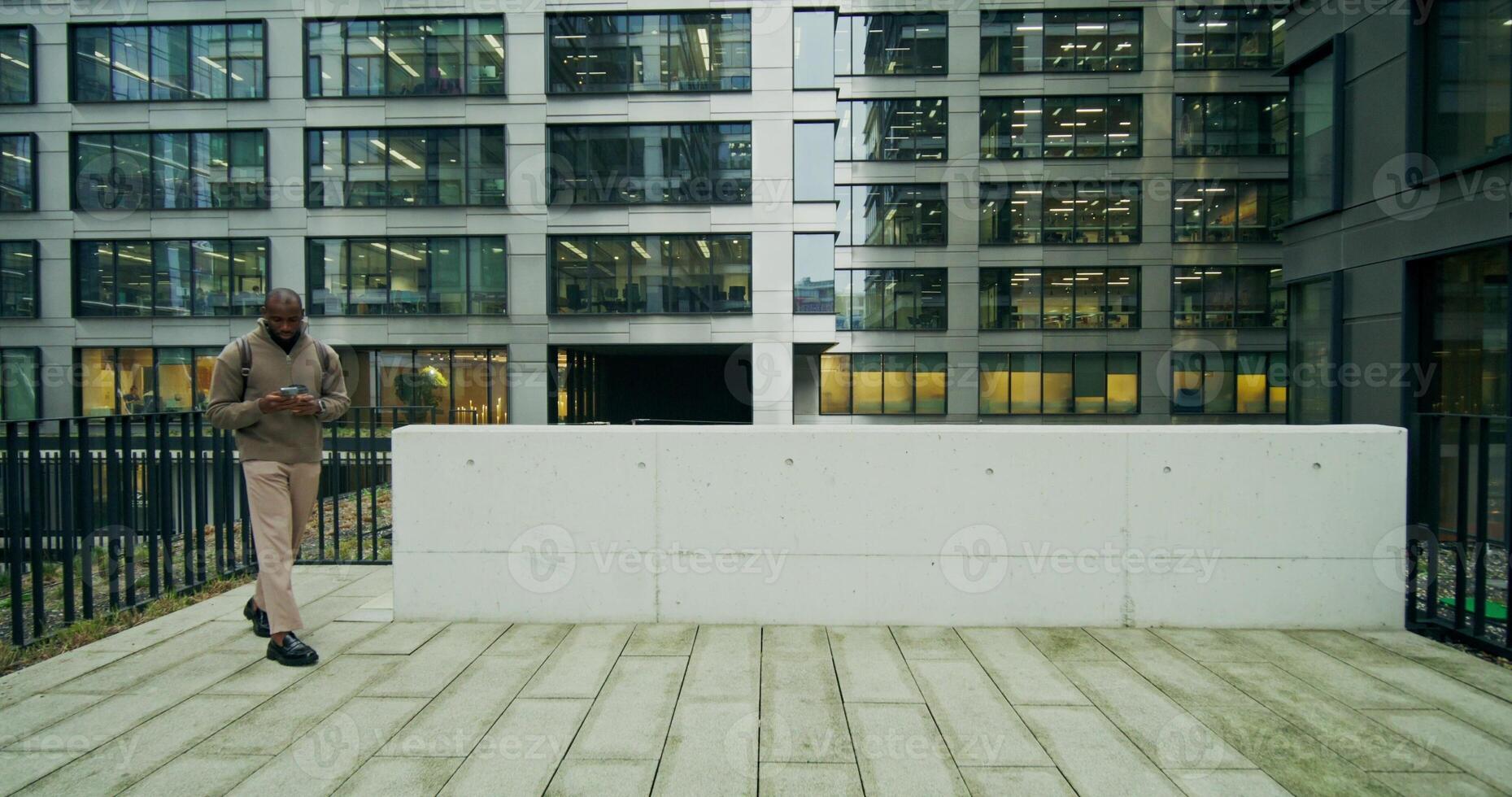 A man in a sweater, with a briefcase on his shoulders, is talking on a mobile phone standing near a city building with a cup of coffee in his hand - mobile photo