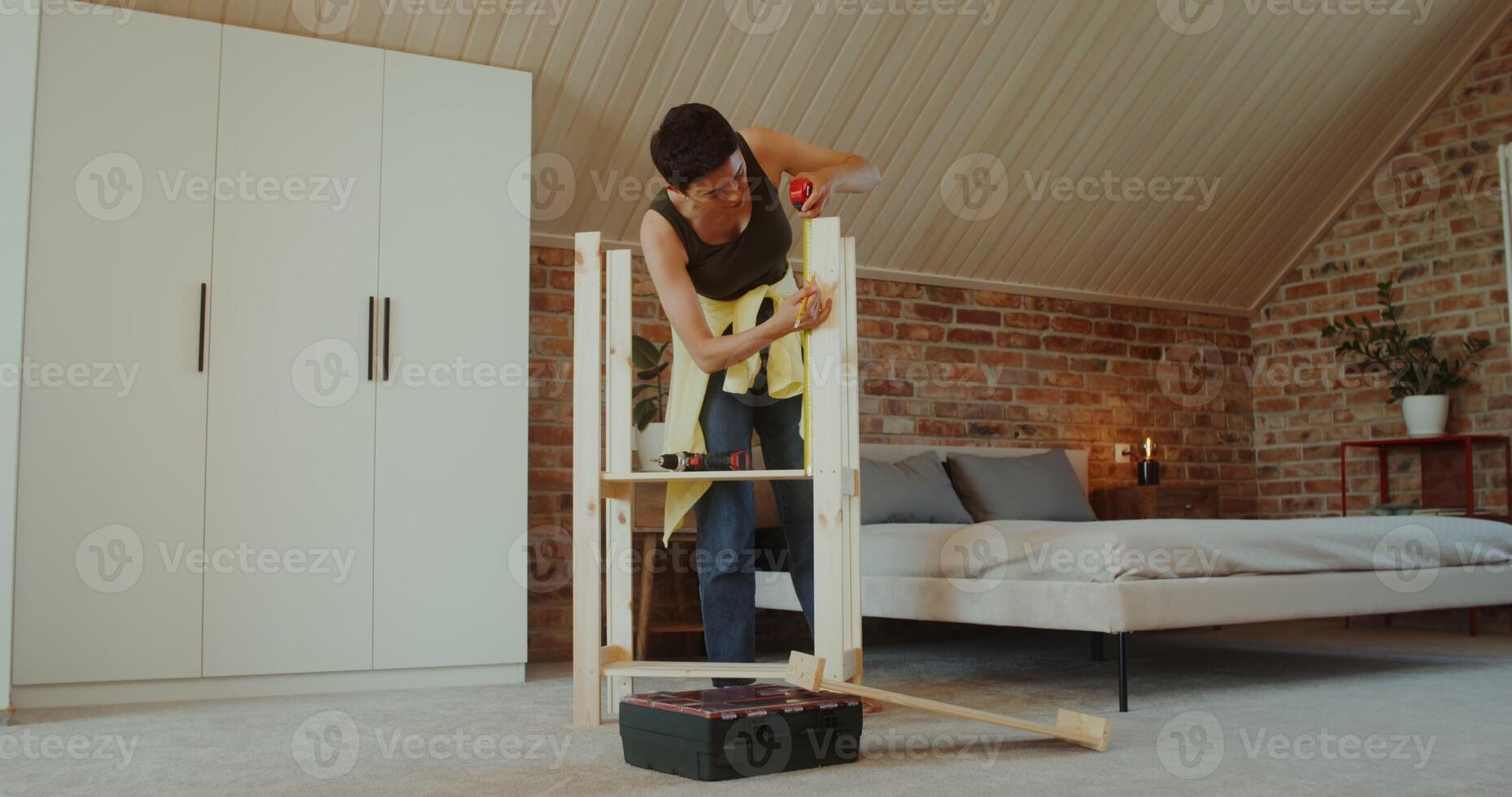A young woman in casual clothes assembles a rack at home using a tape measure photo