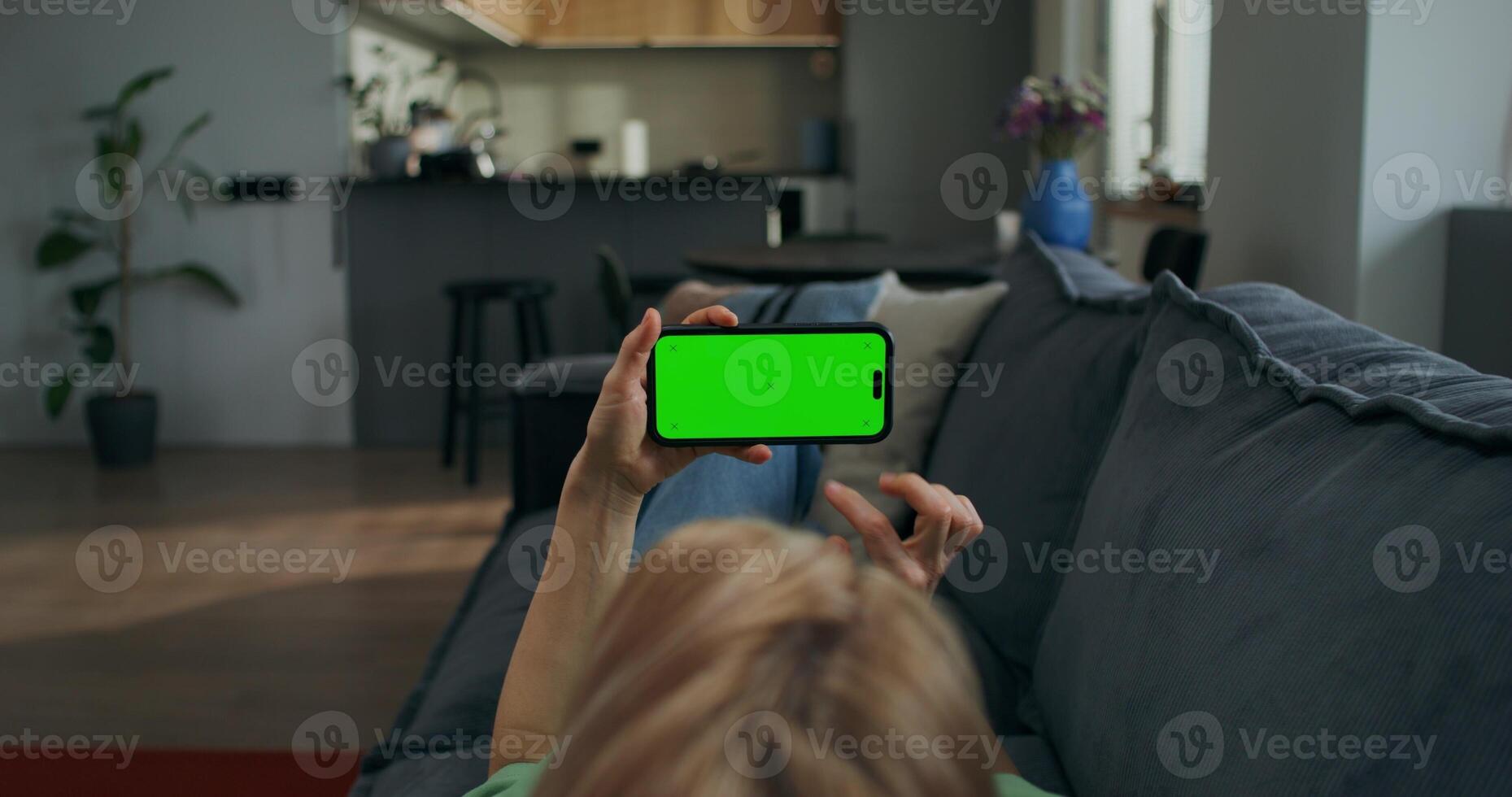 A woman holds a mobile phone with a green screen horizontally in her hands watching , rear view, an unrecognizable person photo
