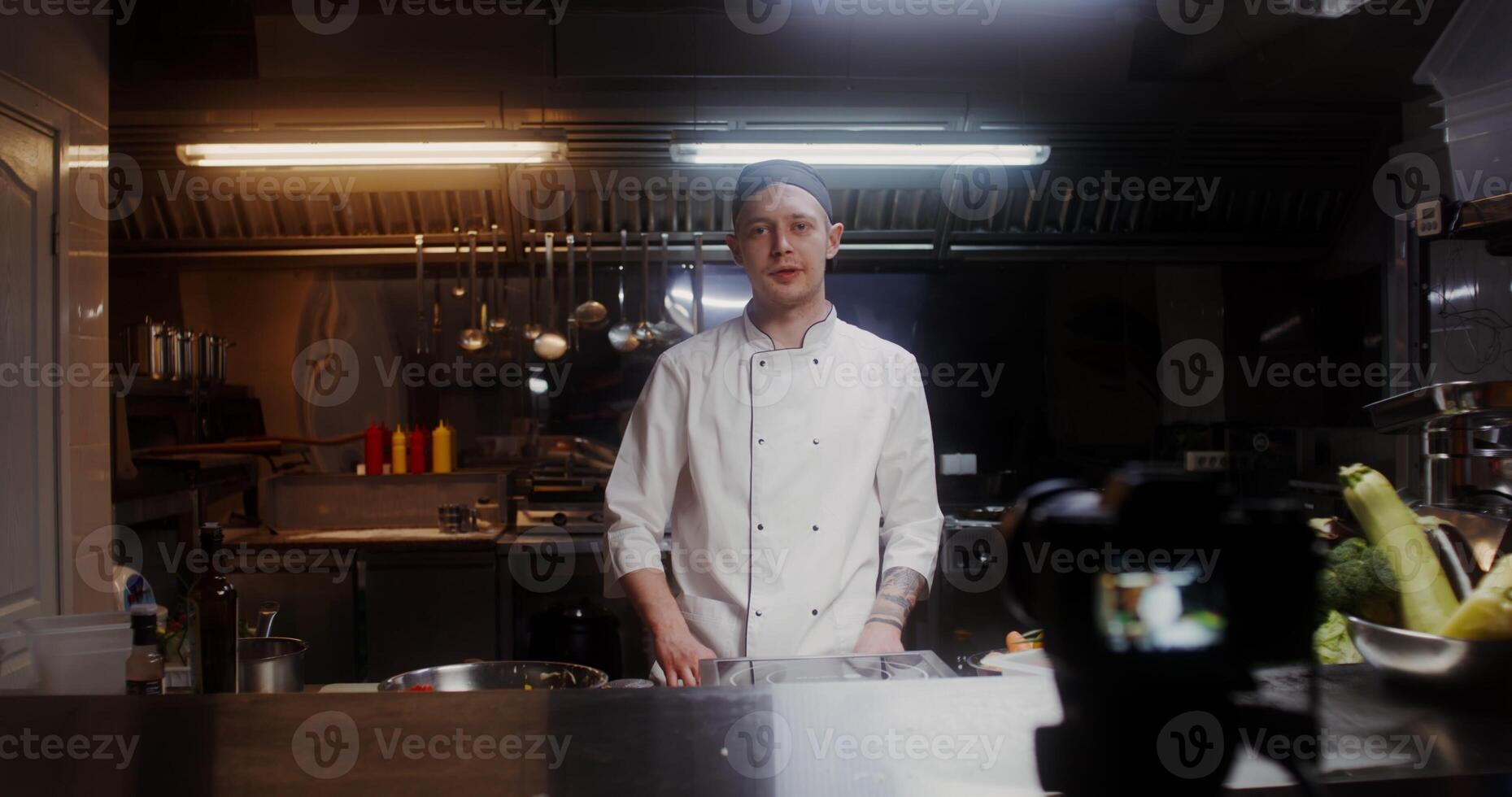 A man in a chef's uniform records the cooking process on , standing near a frying pan in the kitchen of a restaurant - cooking photo
