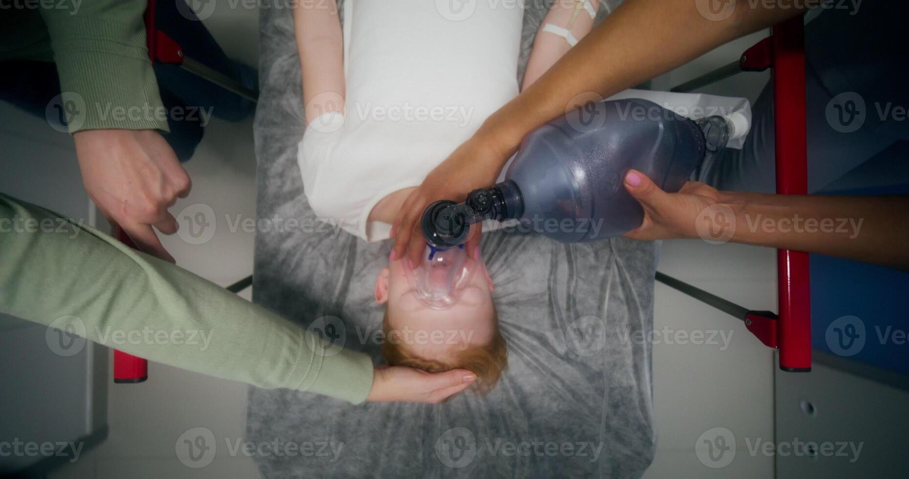 Medical staff and parents carry the boy on a gurney, giving him oxygen with a mask, an overhead view of his face photo
