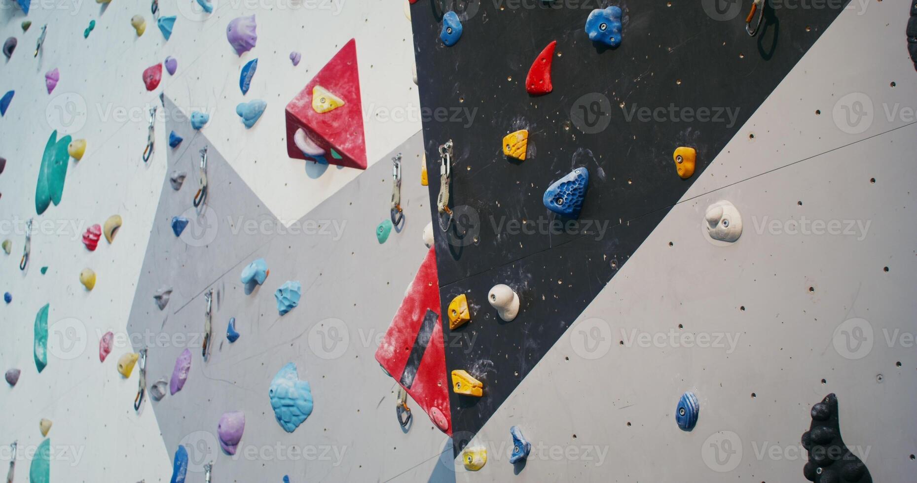 A young man of European appearance, wearing a safety belt, is concentratedly climbing up the climbing wall, grabbing the artificial ledges imitating stones - safety photo