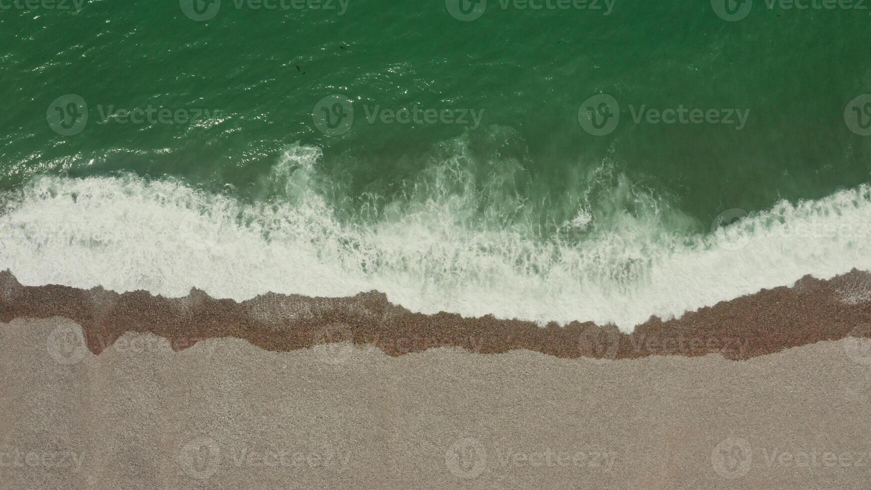 Top view of the sea shore. Emerald water with foam washes a shallow pebble beach, drone . photo