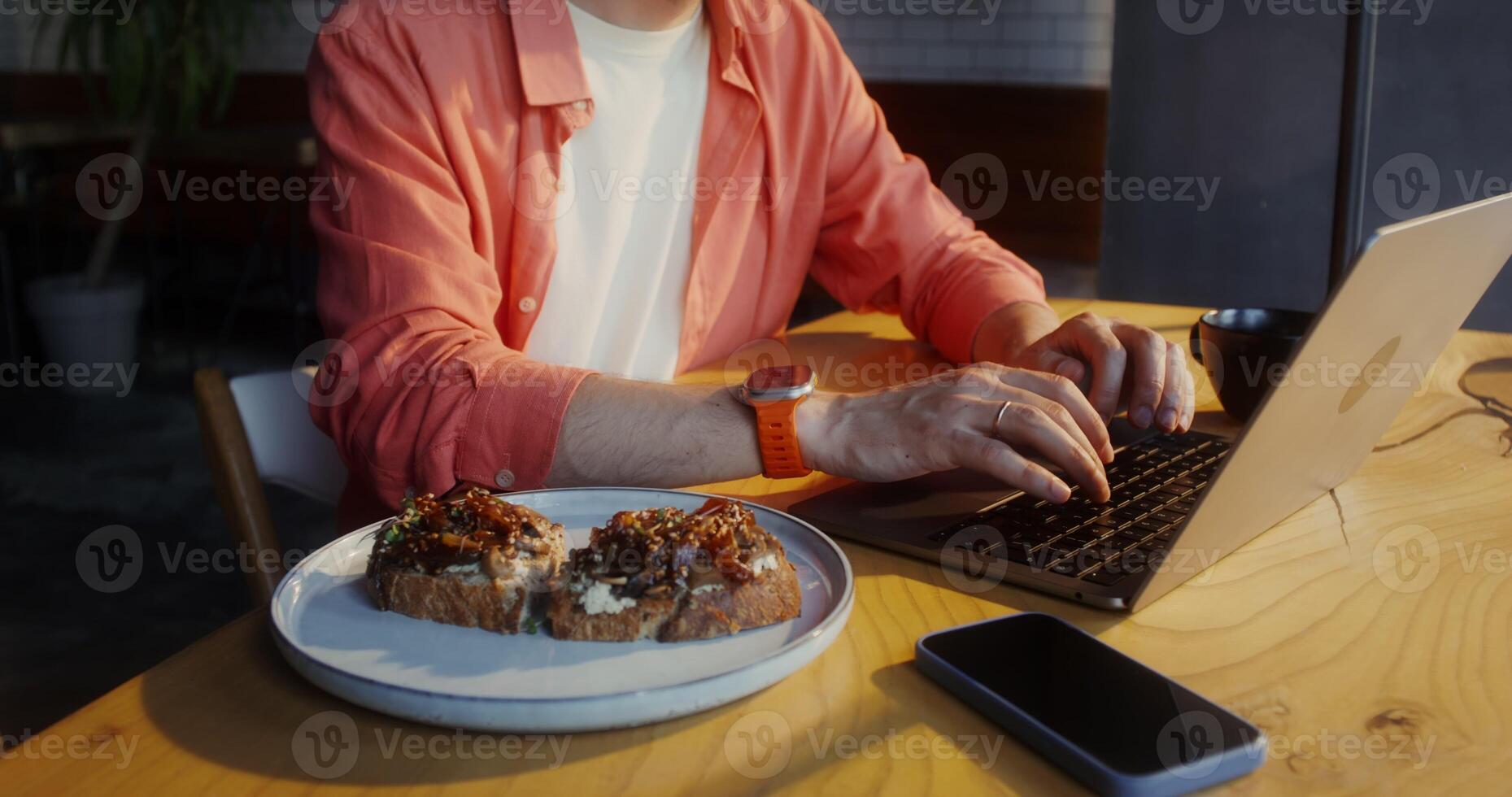 A stylishly dressed man uses a laptop while sitting at a table in a cafe, a close-up of men's hands, no face photo
