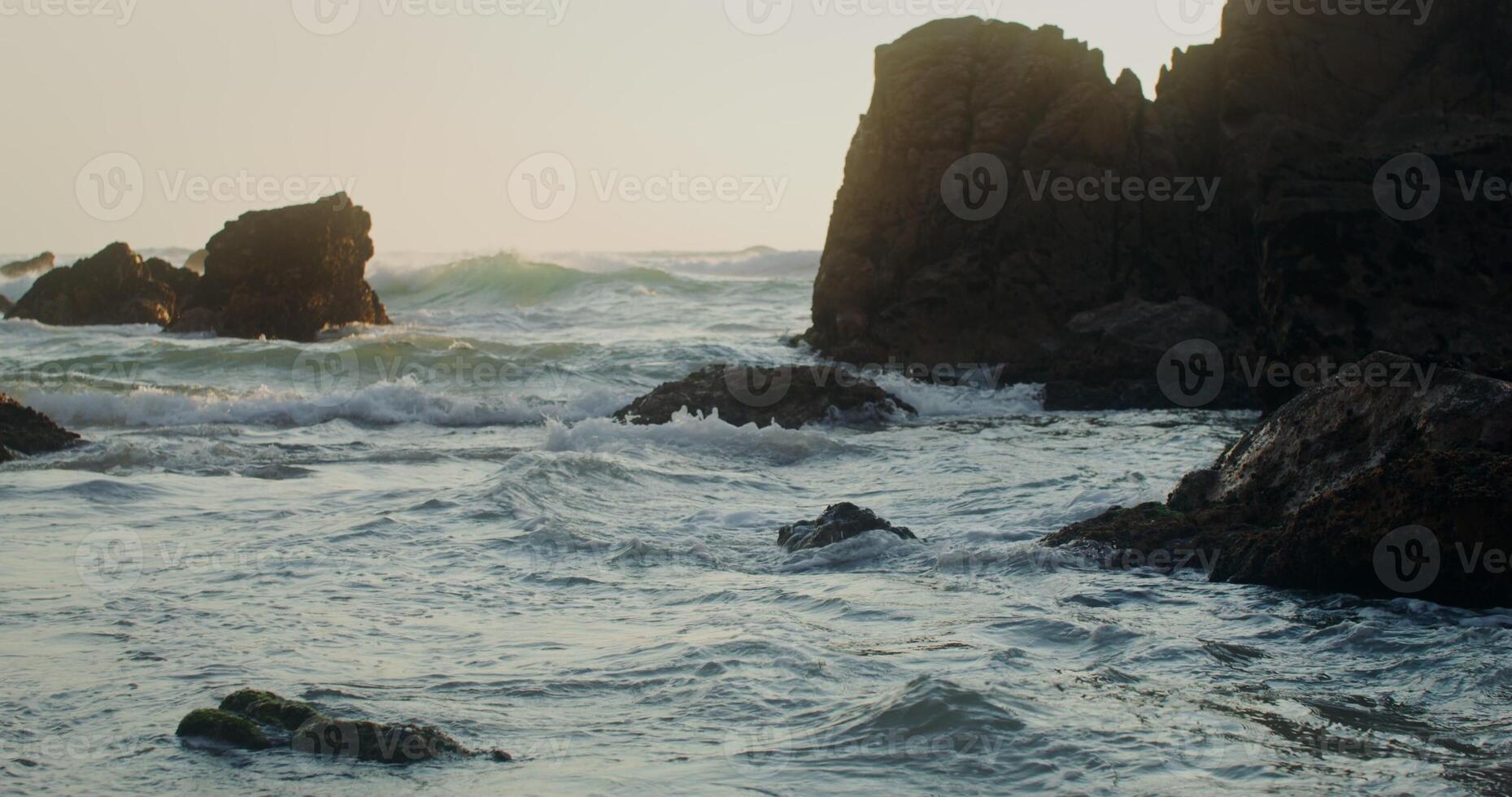 Foamy sea waves beat against the rocks on the shore at sunset photo