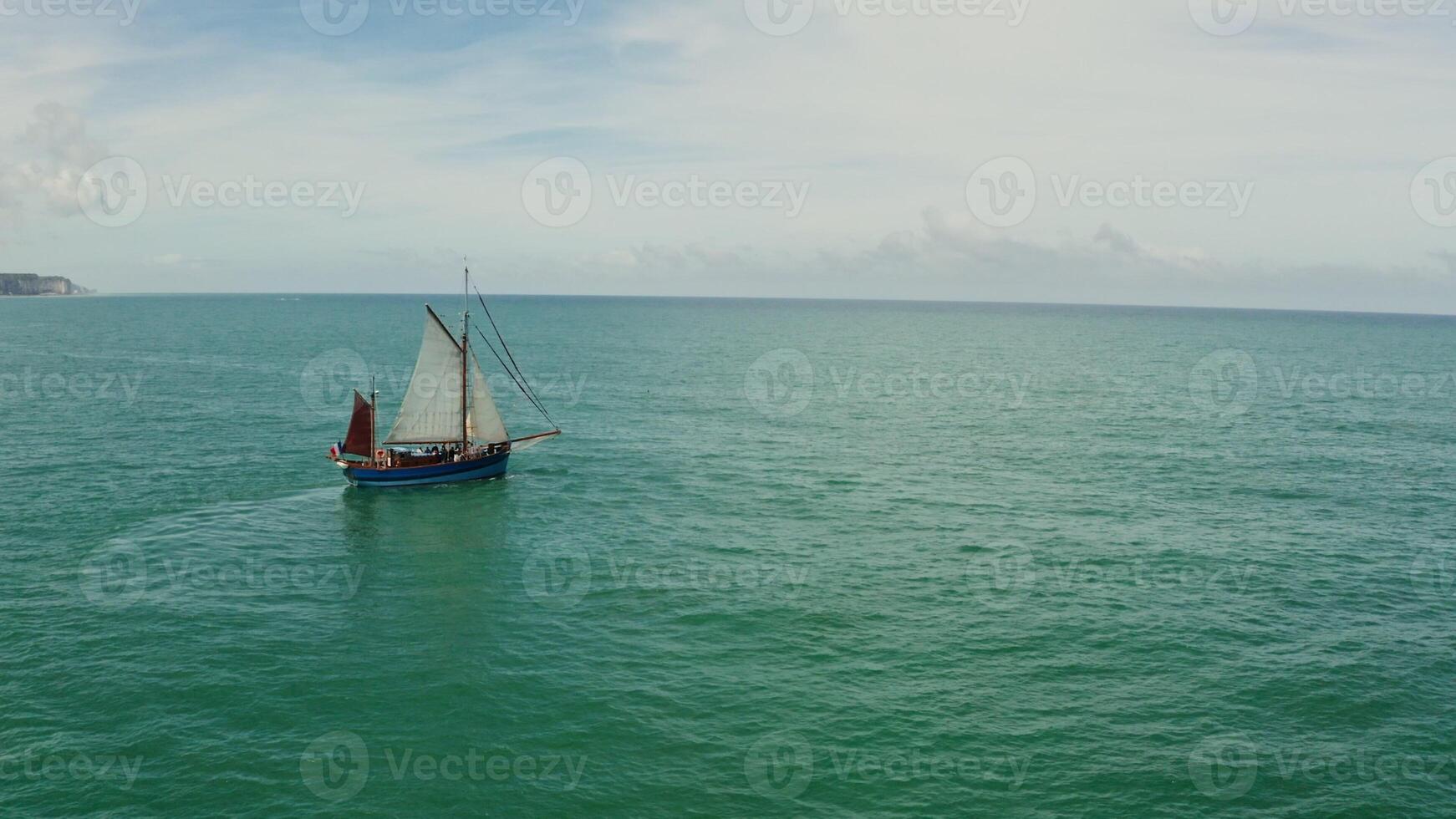 The sailing ship moves away from the land with sheer cliffs along the coast towards the open sea. Drone bird's eye view , Etretat, France photo