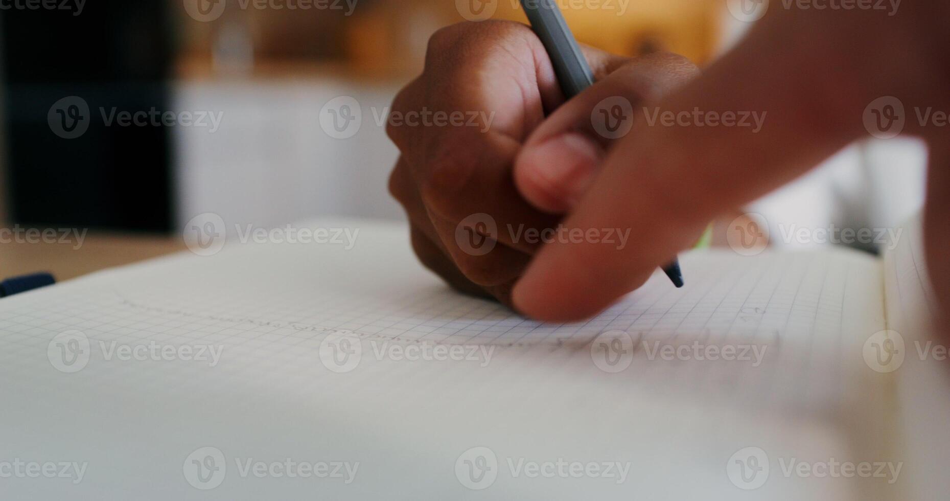A child's hand is writing in a notebook, a girl is doing homework sitting at a table in the kitchen, close-up of her hand photo