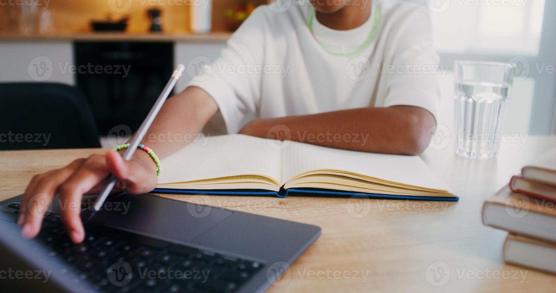 The girl does her homework at home, she uses a laptop and makes notes in a notebook while sitting at the kitchen table. Close-up of a girl's hands - notebook photo