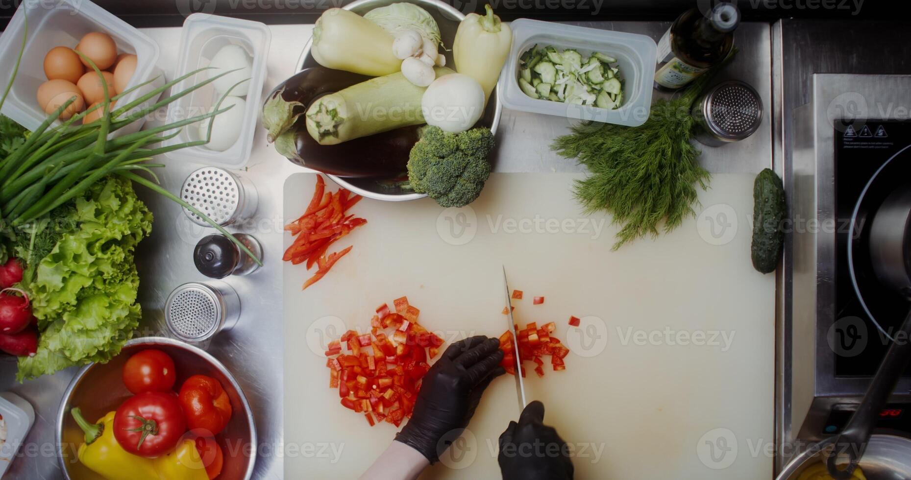 A woman in disposable black gloves cuts peppers standing near a table full of vegetables, close-up of her hands, top view photo