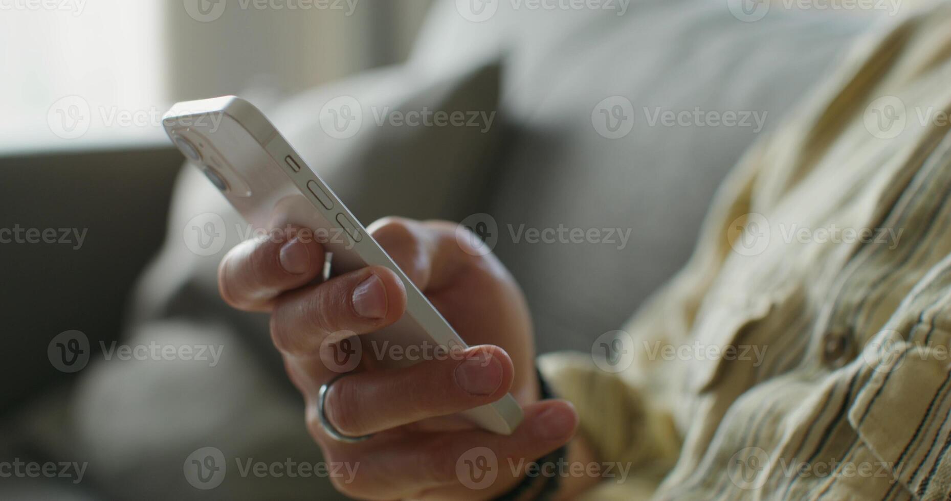 A man is typing on a mobile phone sitting on the couch at home. close-up of his hands, an unrecognizable person. Daylight - Daylight photo