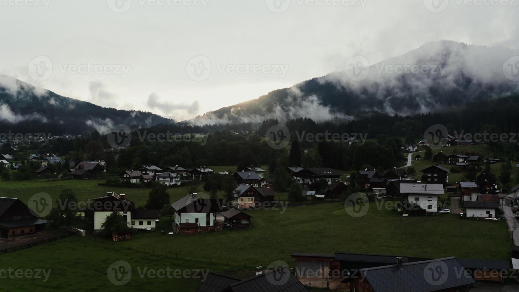 The sun rising from behind the mountains illuminates a beautiful mountain valley with cottage houses in the lowlands and green gentle hills covered with fluffy white clouds. Austria, Alps - mountains photo