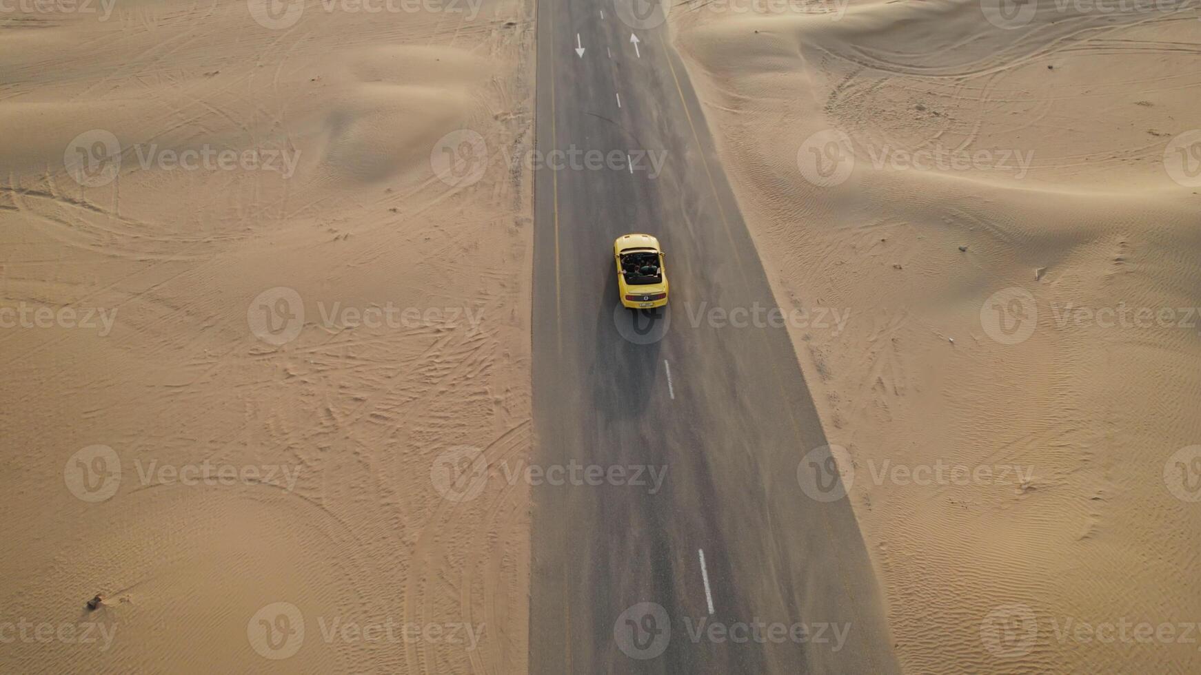 The drone flies over a yellow convertible driving along the road past the sand dunes of the desert - desert photo