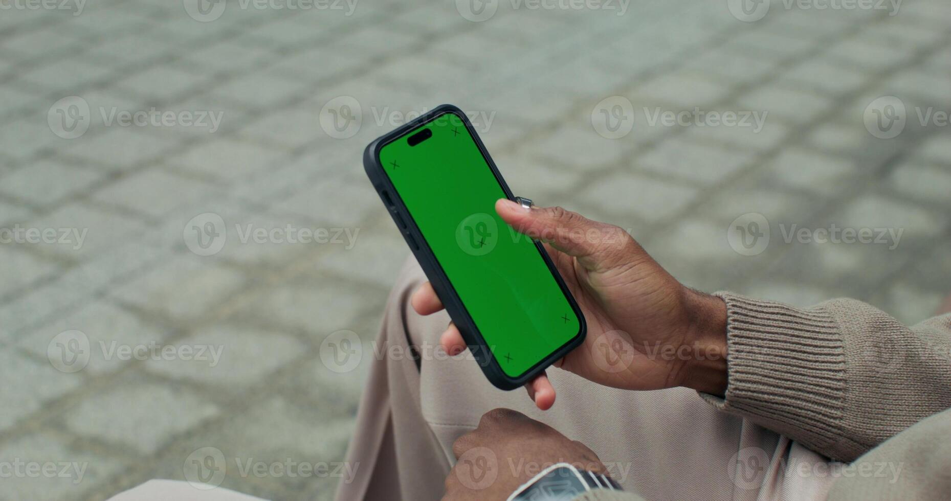 A man uses a mobile phone with a green screen sitting outdoors, close-up of his hands, an unrecognizable person - screen photo