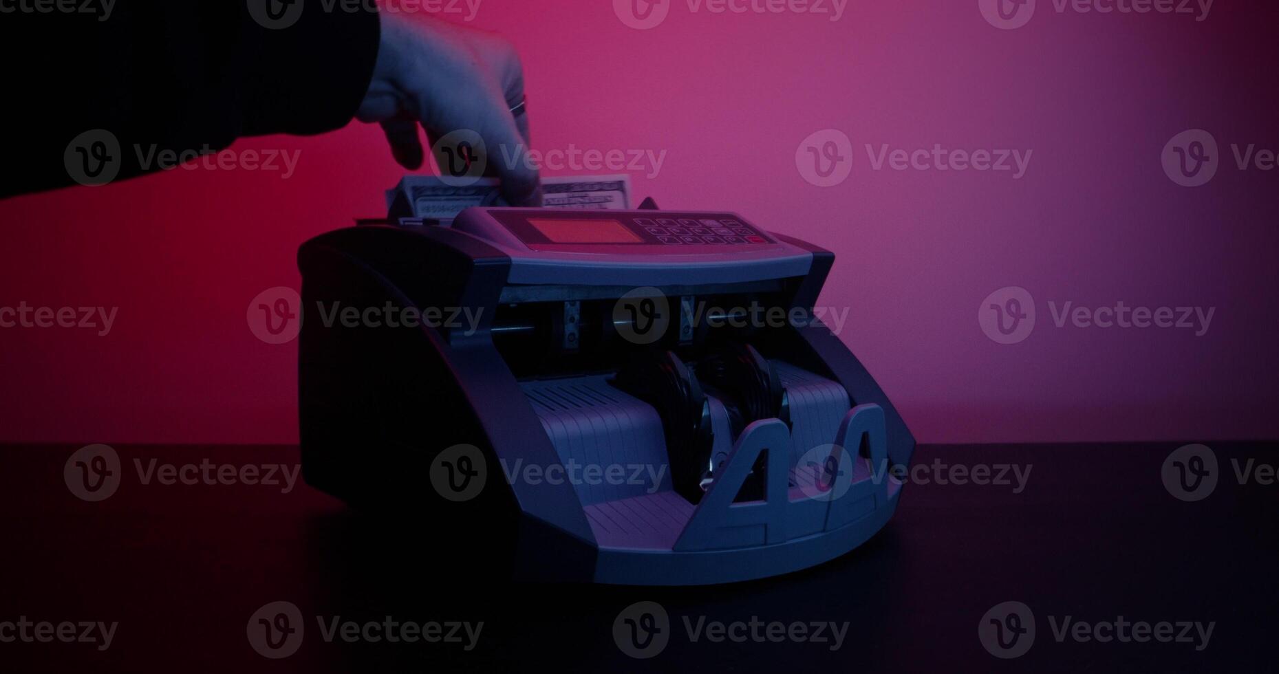 A man's hand inserts a stack of hundred dollar bills into a counting machine and it starts counting, studio photo