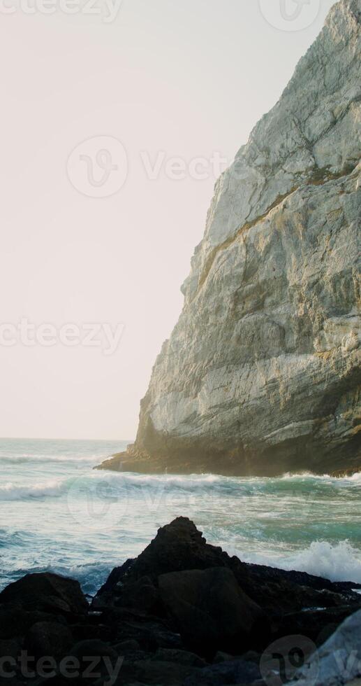 A cliff on the seashore, sea waves beating against a stone - against photo