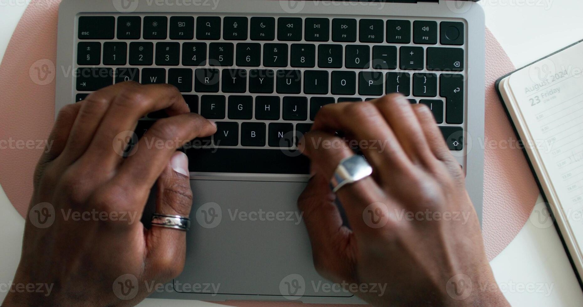A man typing on a laptop, sitting at a table indoors, close-up of his hands, an unrecognizable person, view from above. An open notebook is on the table - unrecognizable photo