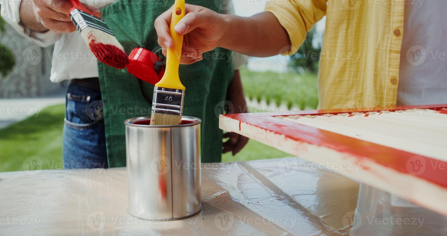 A man in an apron and a boy paint the door in red color while standing in the backyard. Close photo