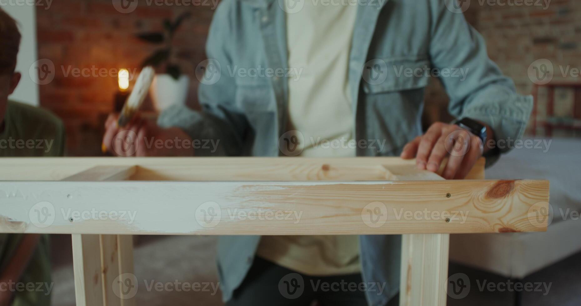 A father and son of European appearance paint a rack using brushes, sitting in a home interior, they smile and talk during vacation photo