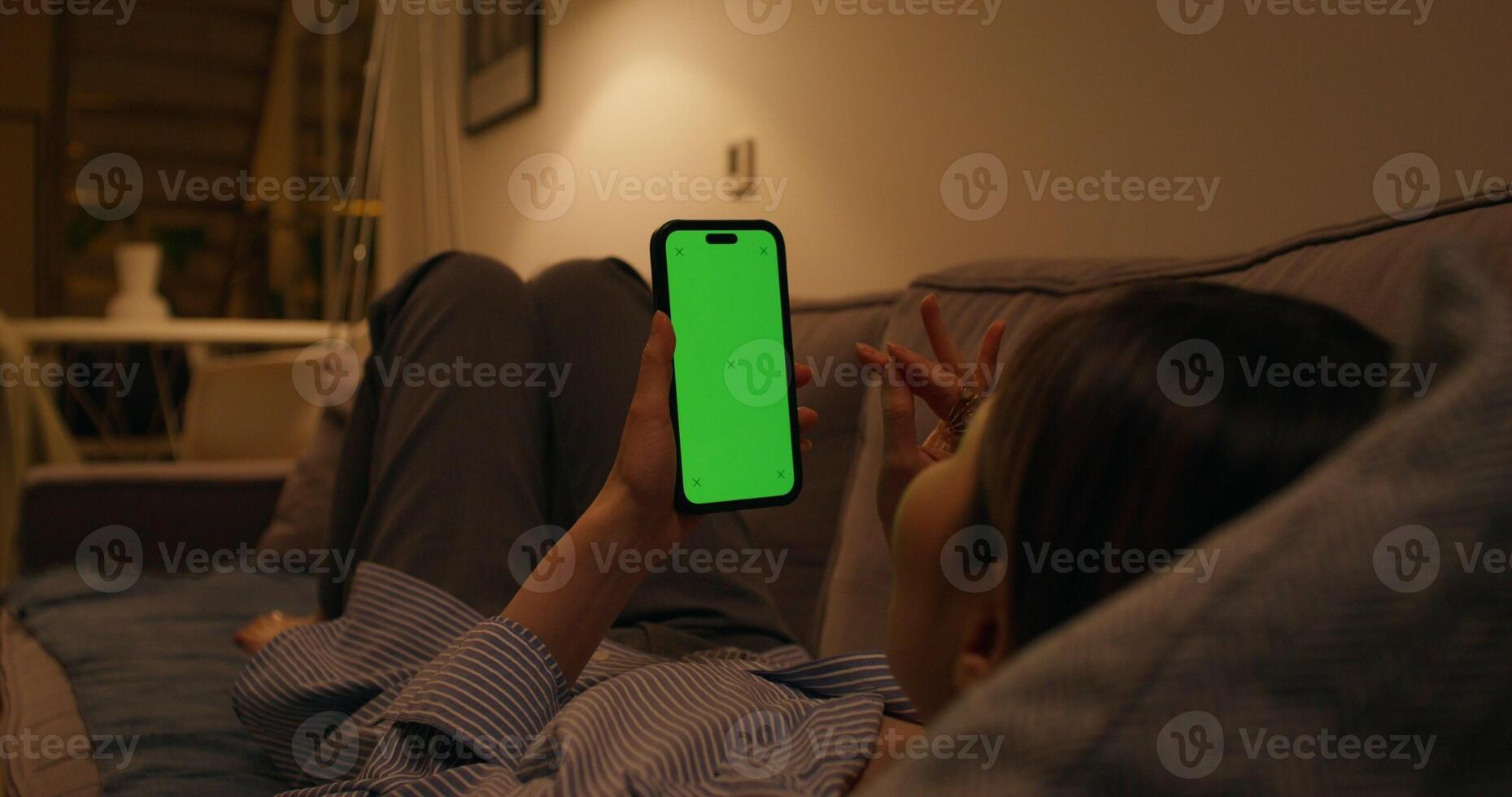 A woman uses a mobile phone with a green screen lying on the couch at home - screen photo