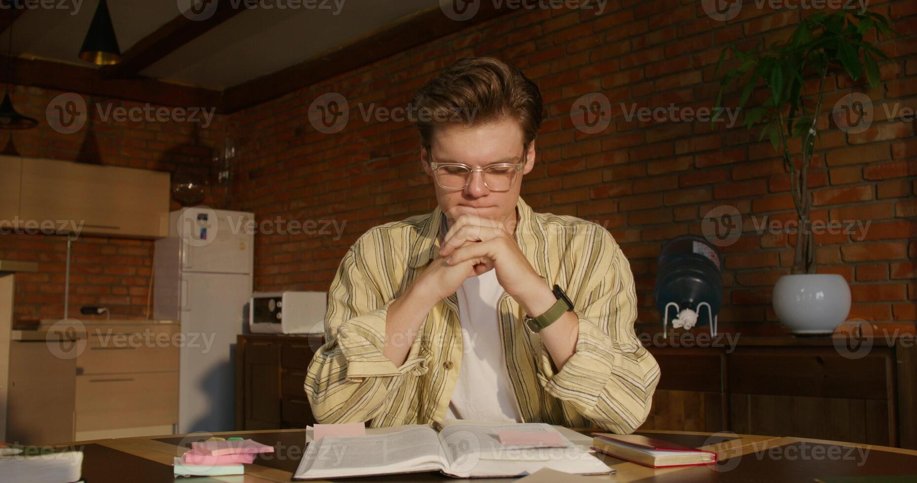 A man is studying the Bible while sitting at a table indoors. He prays with his hands folded in front of him. Daylight - folded photo