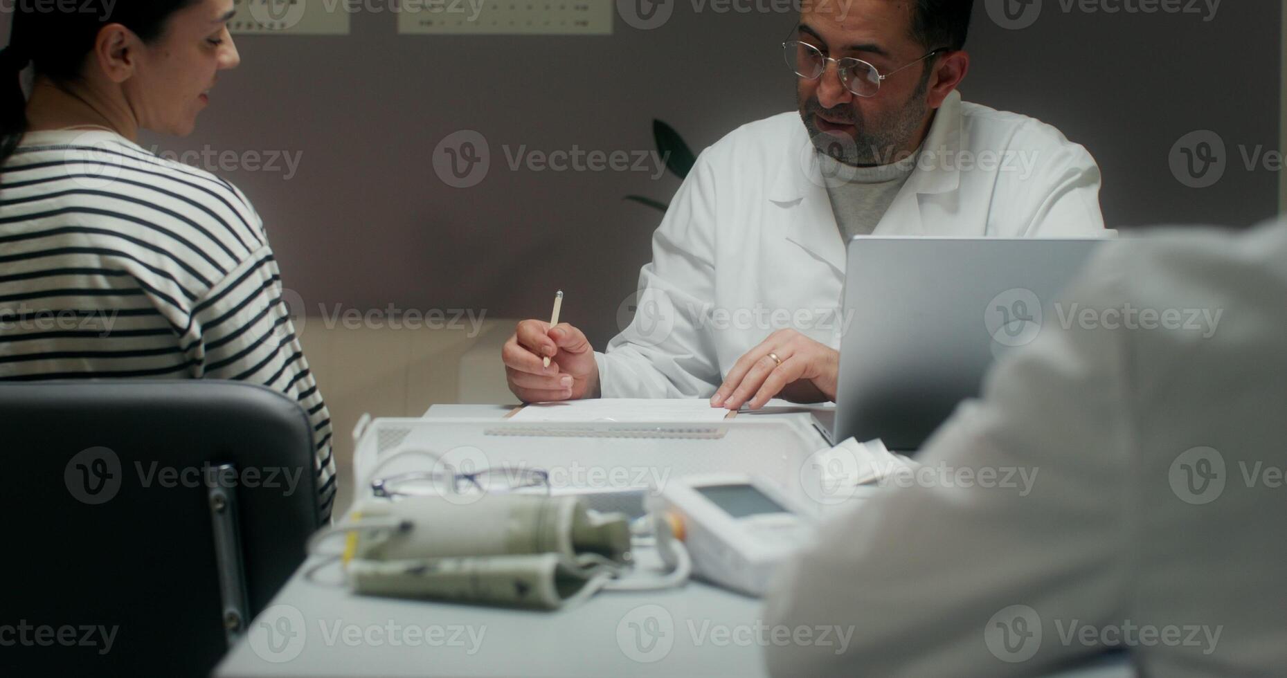 The doctor listens to the patient's complaints sitting in front of an open laptop at the table and writes in a notebook. Medical appointment at the clinic - complaints photo