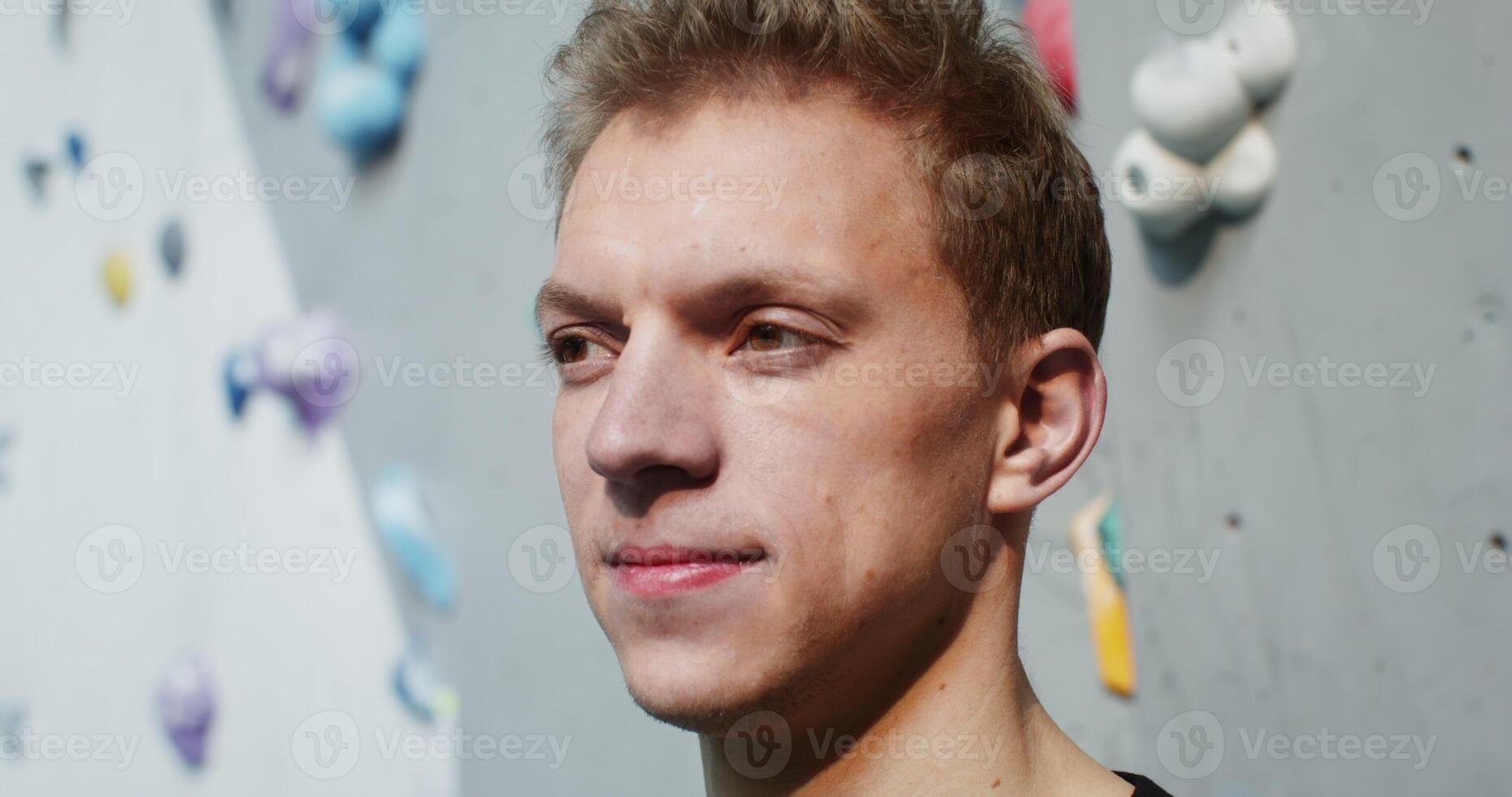 Young man of European appearance smiling looking straight into the camera, standing in front of a climbing wall in an indoor hall, close-up - smiling photo