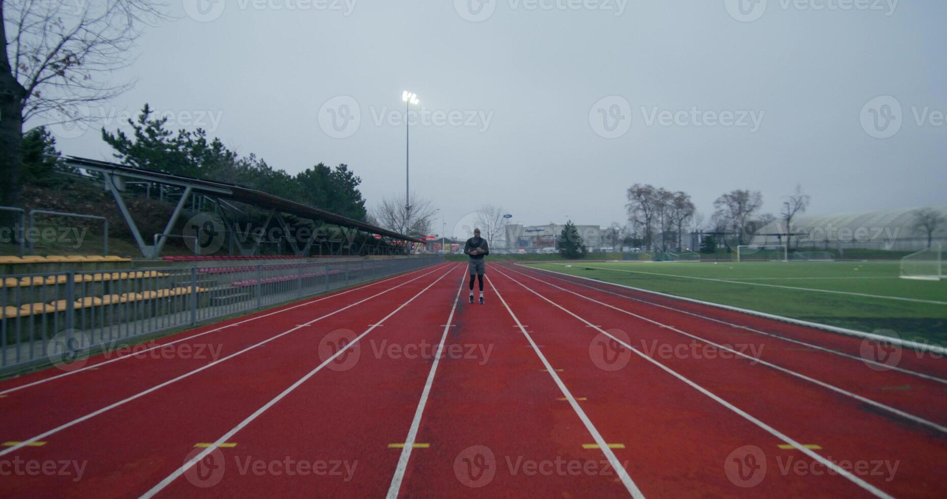 A man in sports clothes runs around the stadium on a cold day alone, front view - stadium photo