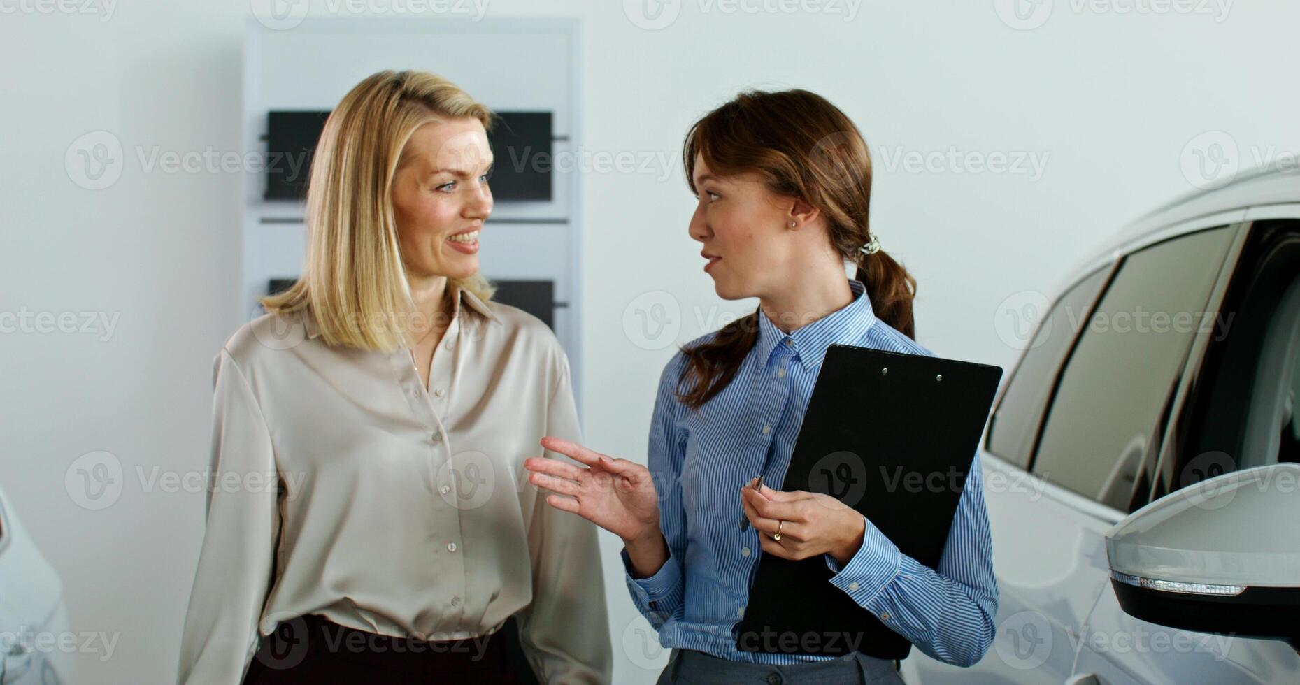 A stylish woman chooses a car at a car dealership. The manager talks to the client showing the cars - chooses photo