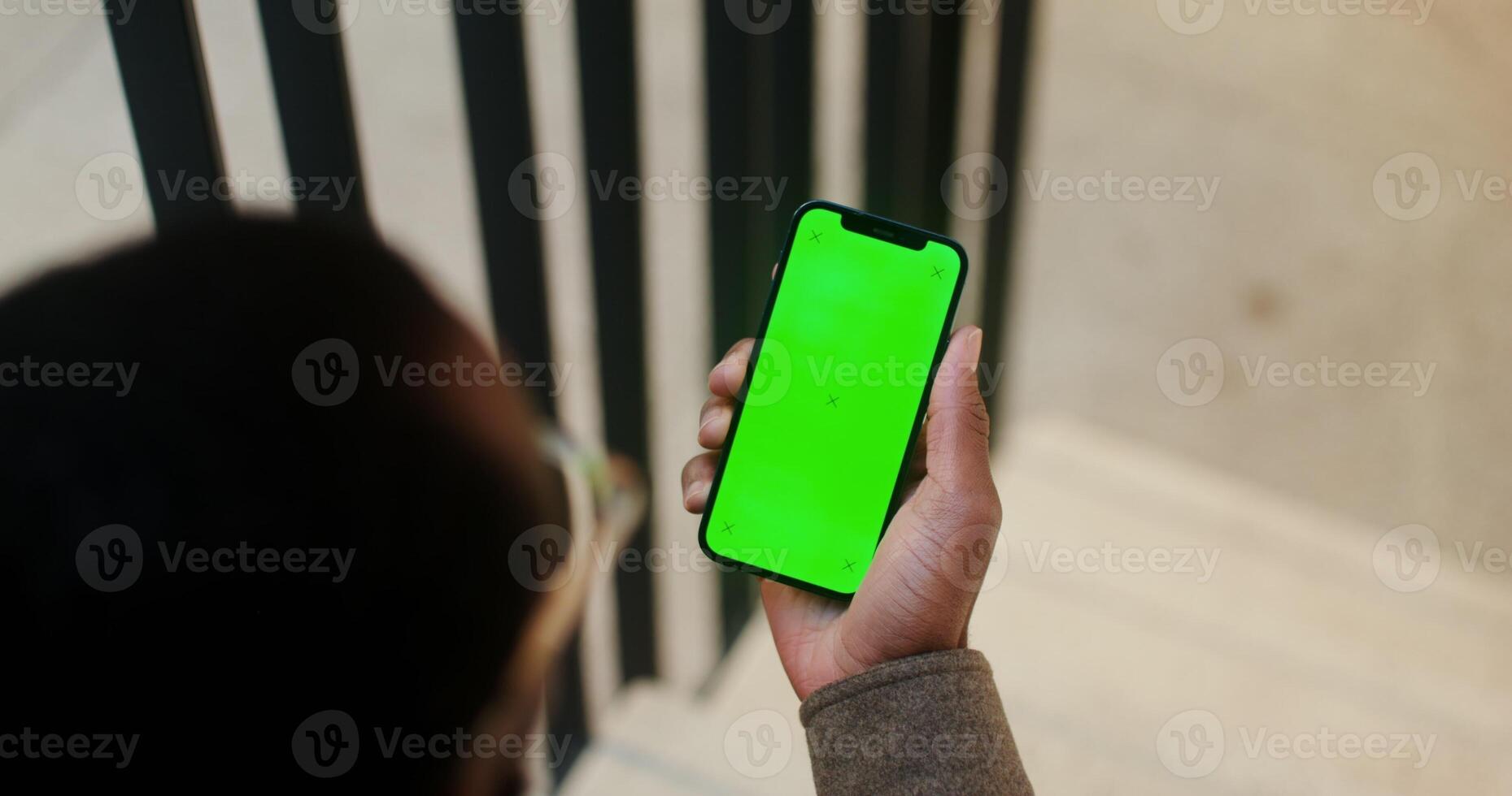 An African American man holds a mobile phone with a green screen in his hand. filming from behind, his face is not visible. Copy space, mockup, chroma key. in 4k, red komodo - mobile photo