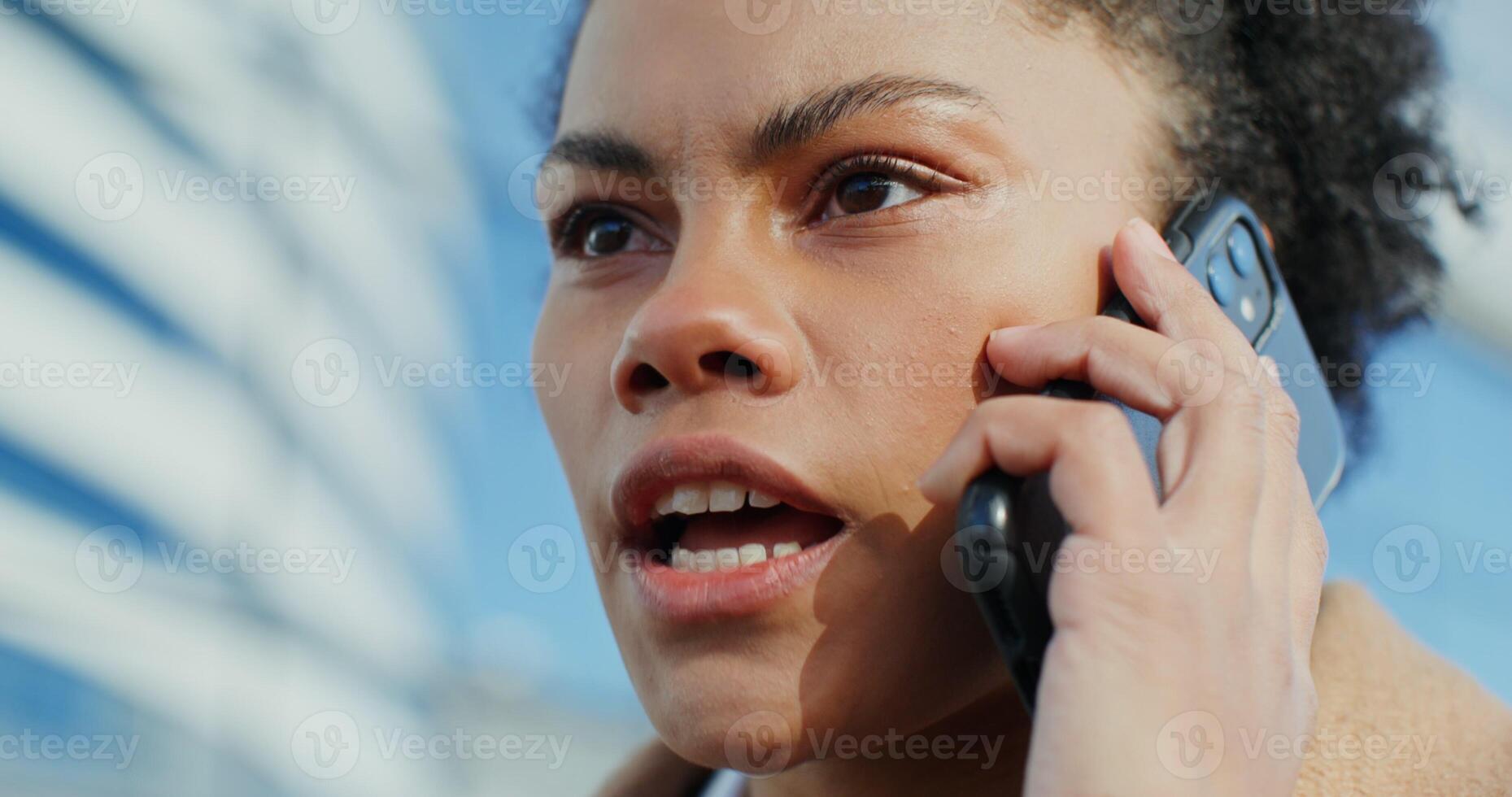 Beautiful young african american woman swearing while talking on a mobile phone outdoors, close-up - american photo